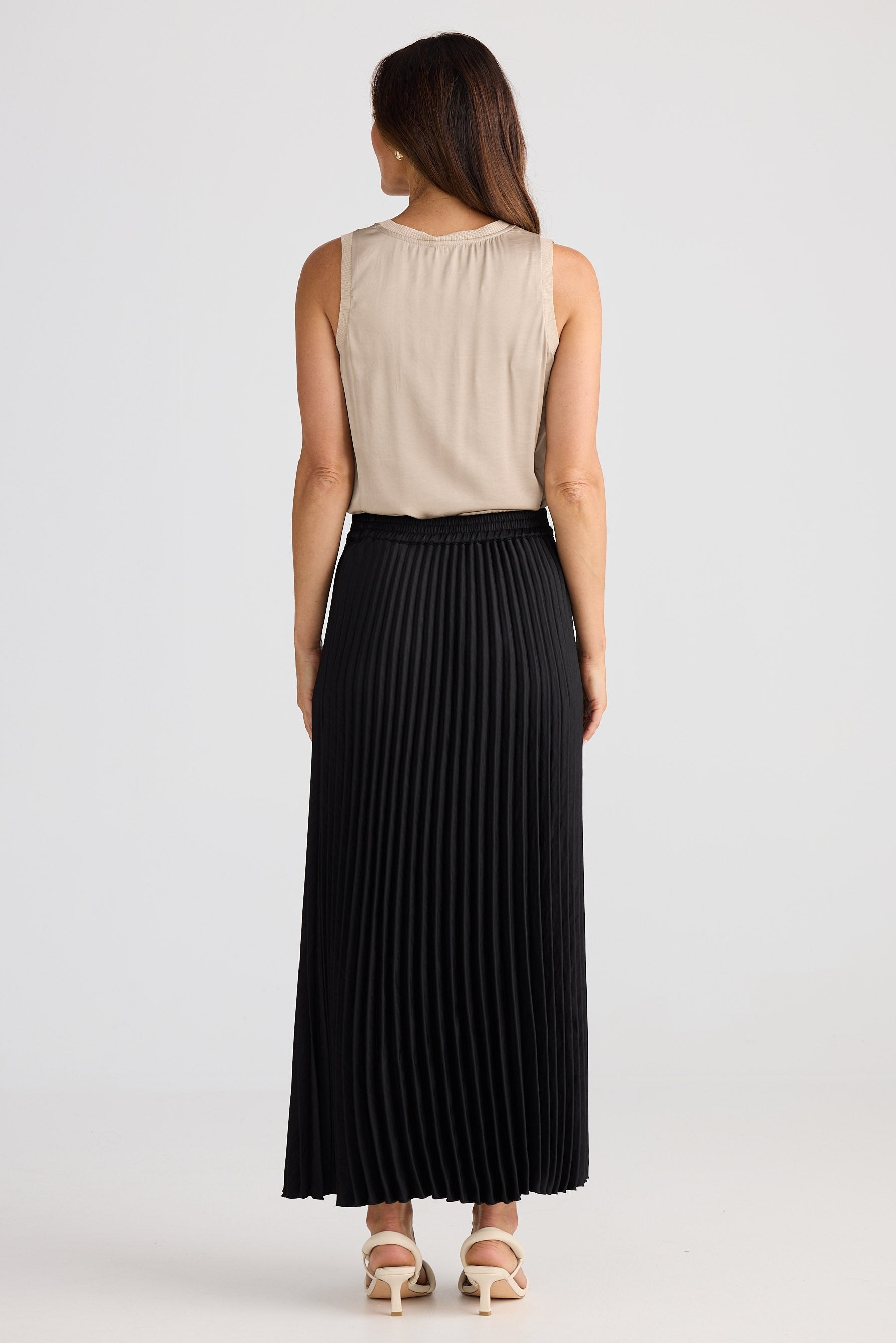 Woman wearing a beige sleeveless top and black pleated skirt on a white background