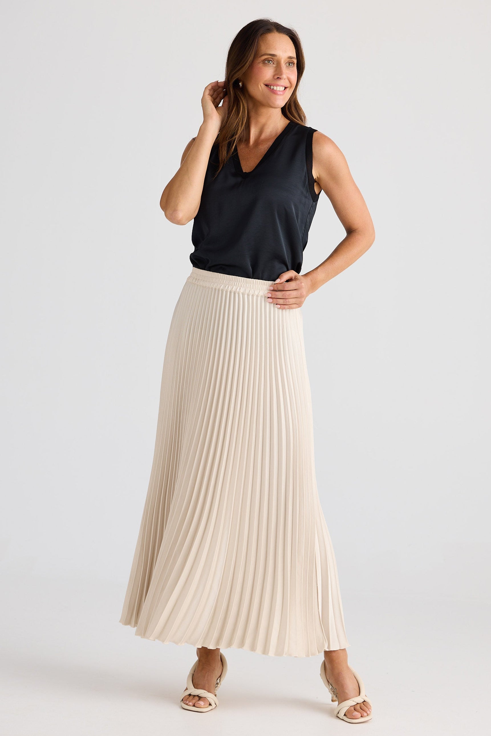 Woman wearing a black sleeveless top and beige pleated skirt on a white background