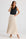 Woman wearing a black sleeveless top and beige pleated skirt on a white background