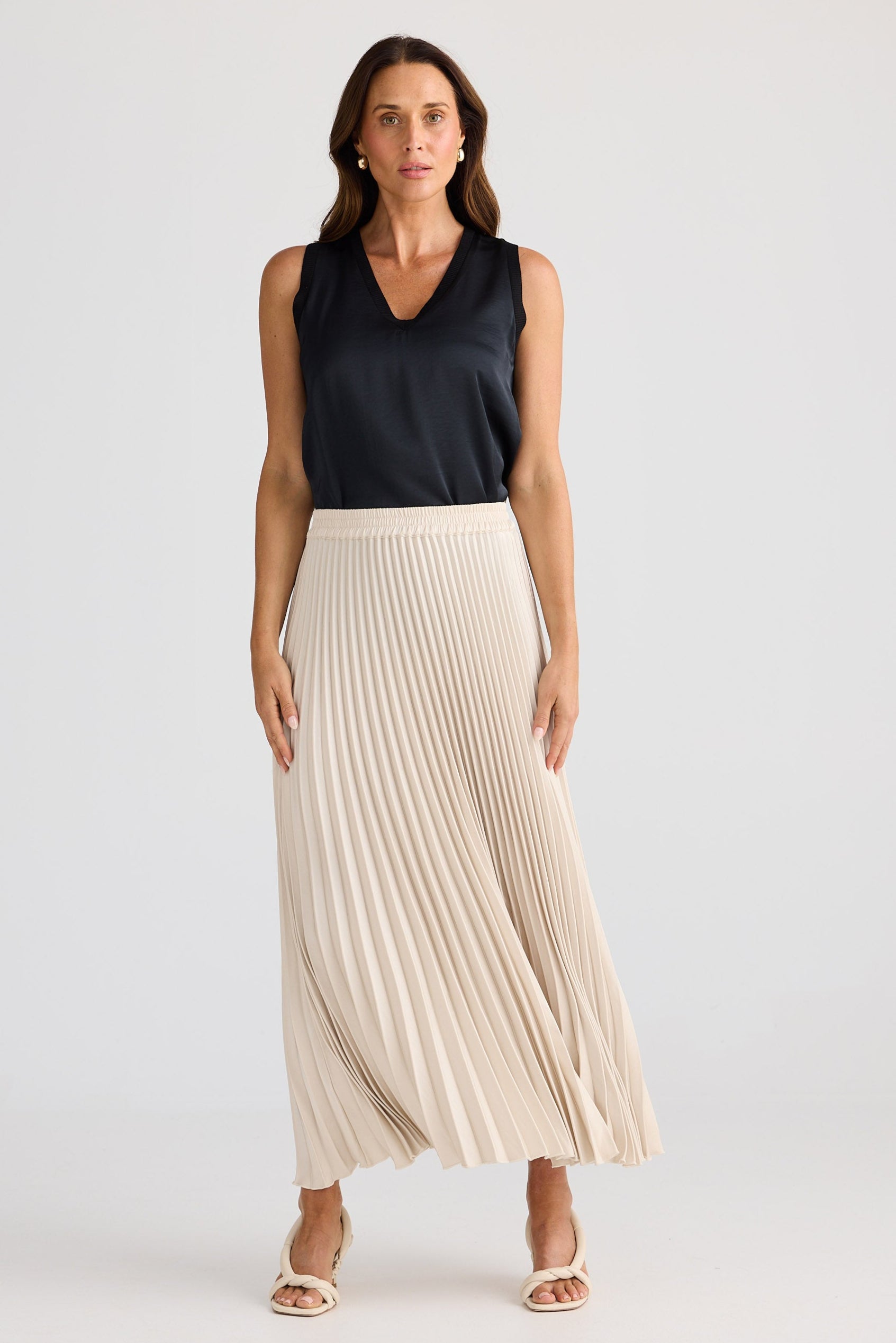 Woman wearing a black sleeveless top and beige pleated skirt on a white background