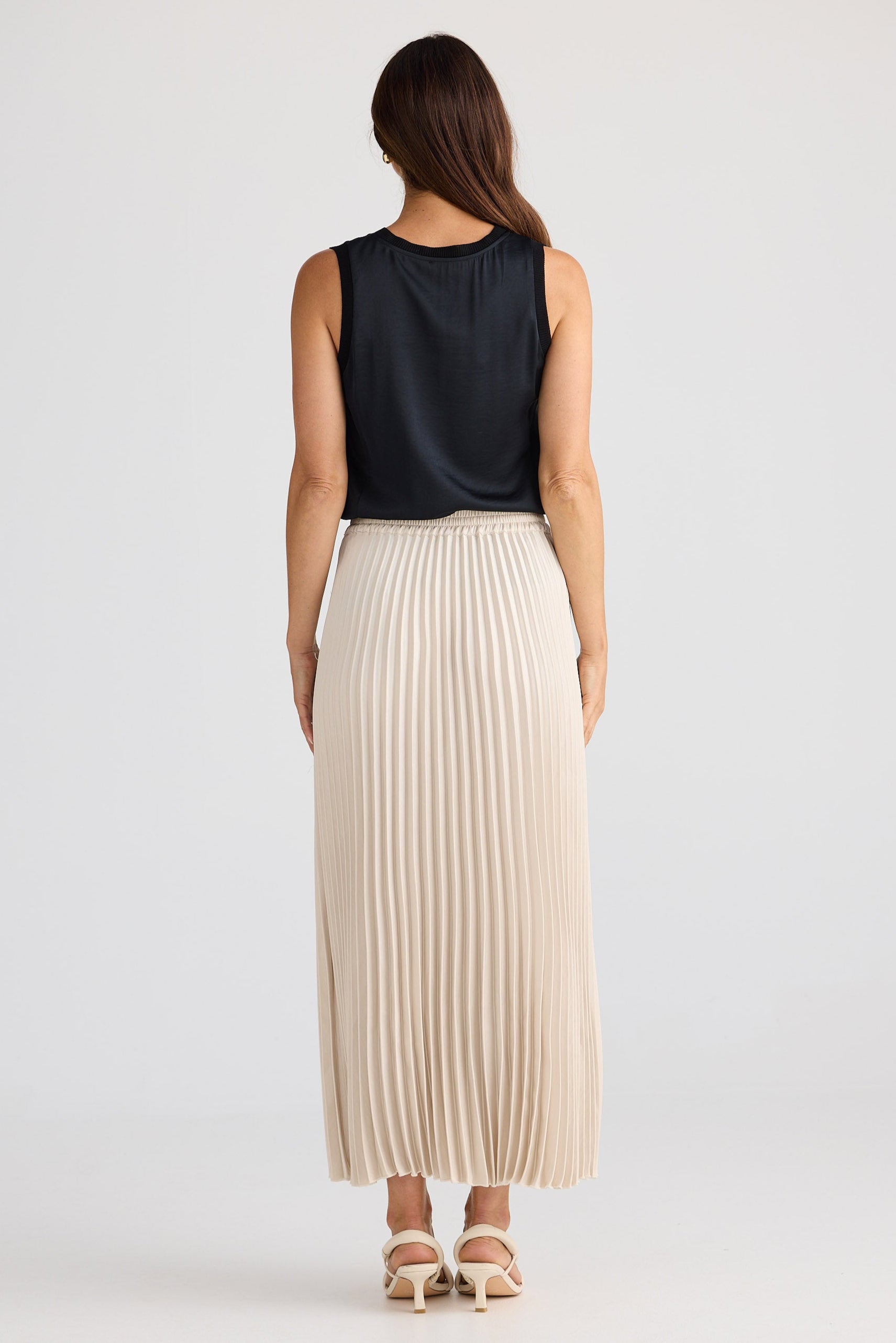 Woman wearing a black sleeveless top and beige pleated skirt on a white background