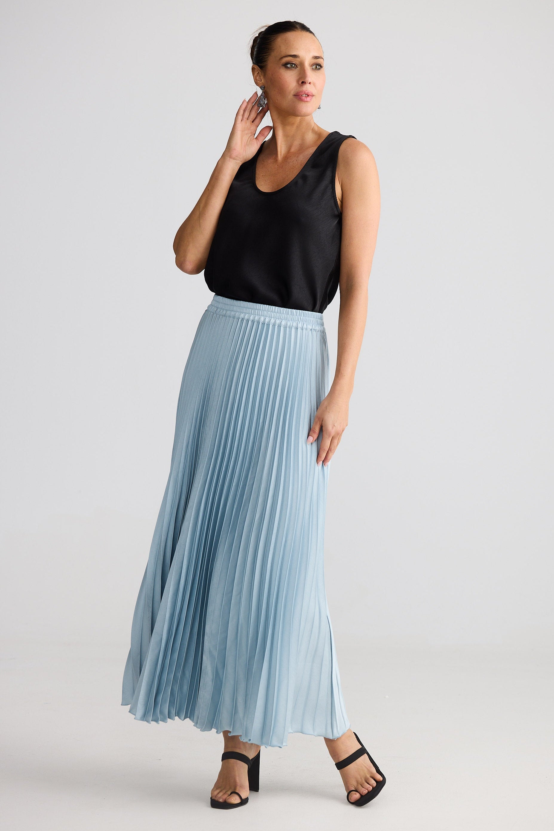 Woman wearing a black sleeveless top and light blue pleated skirt on a white background