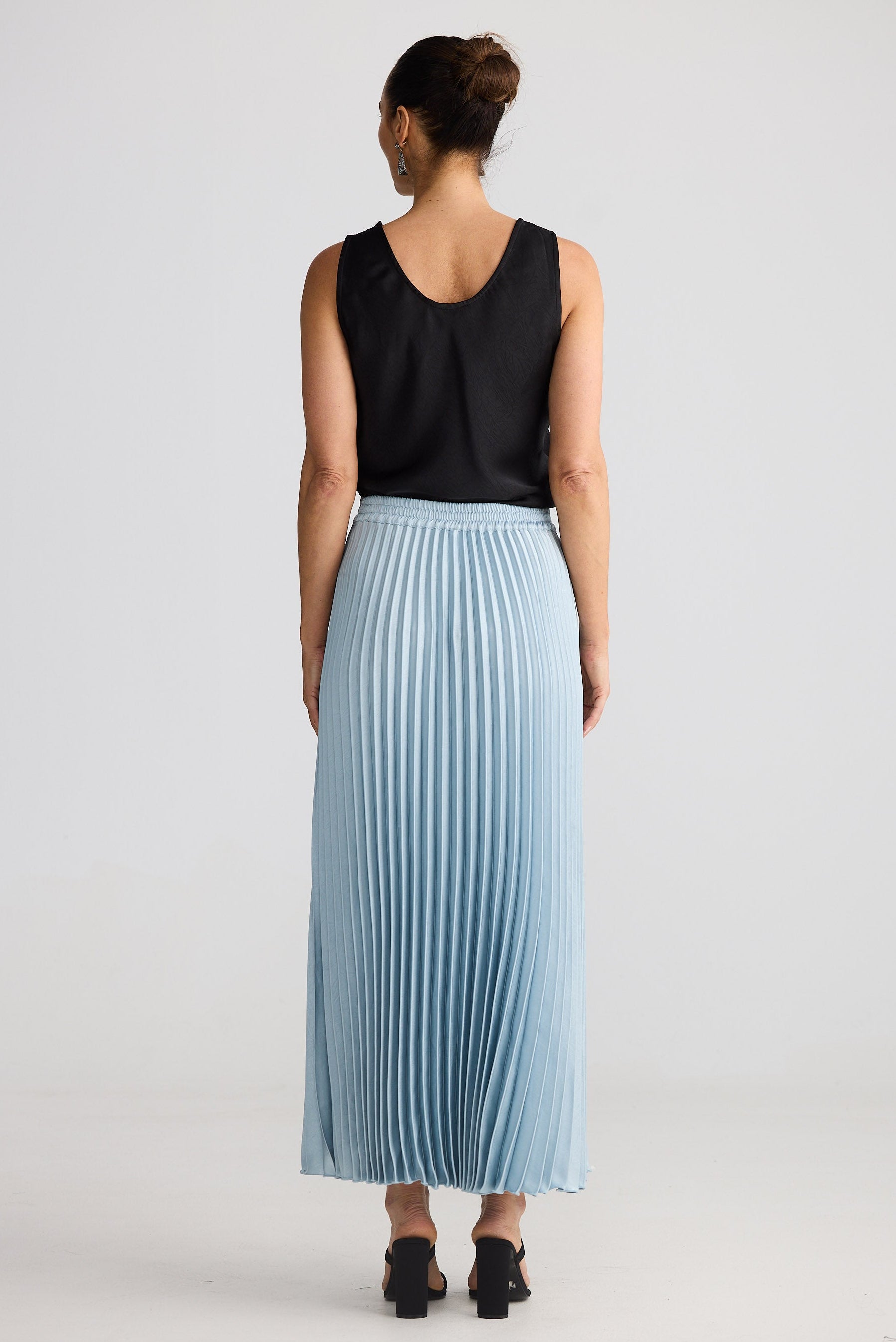 Person wearing a black sleeveless top and light blue pleated skirt on a white background