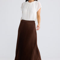 Model wearing Alias Pleated Skirt in chocolate brown by Brave + True, front view.