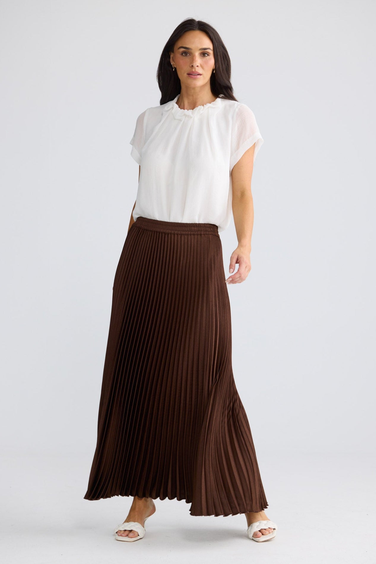Model wearing Alias Pleated Skirt in chocolate brown by Brave + True, front view.
