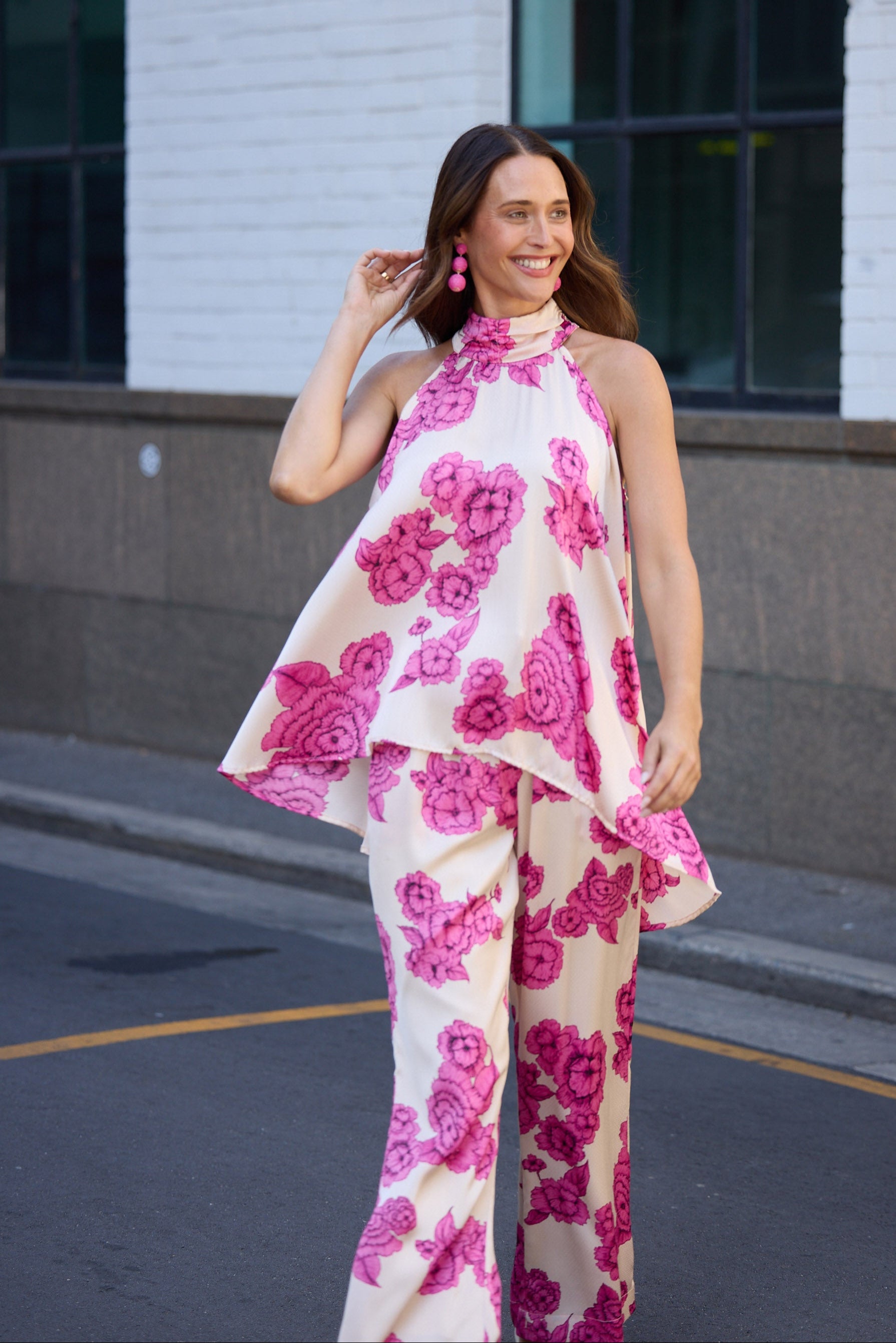 Woman wearing a pink floral dress standing on a street.