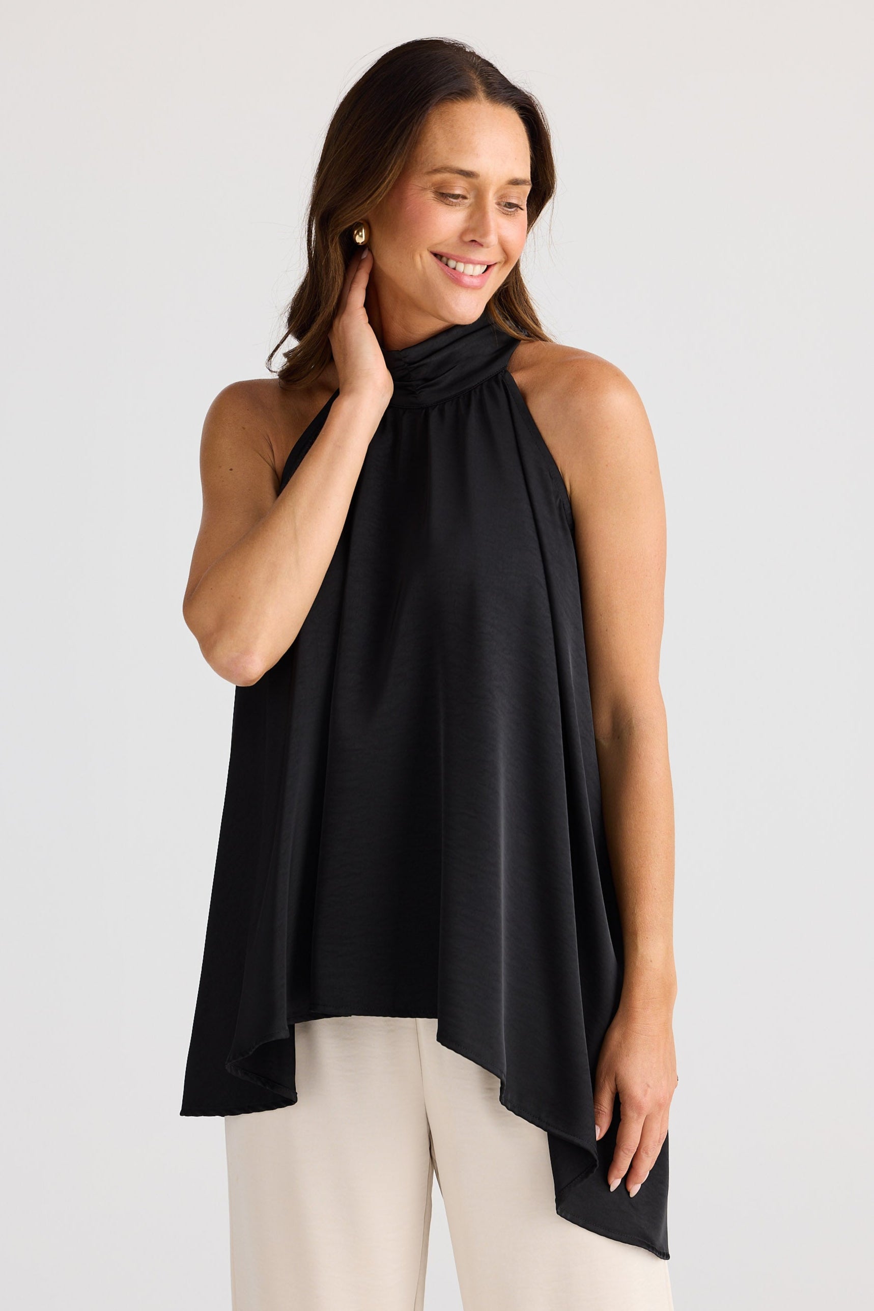 Woman wearing a black sleeveless top and beige pants on a white background