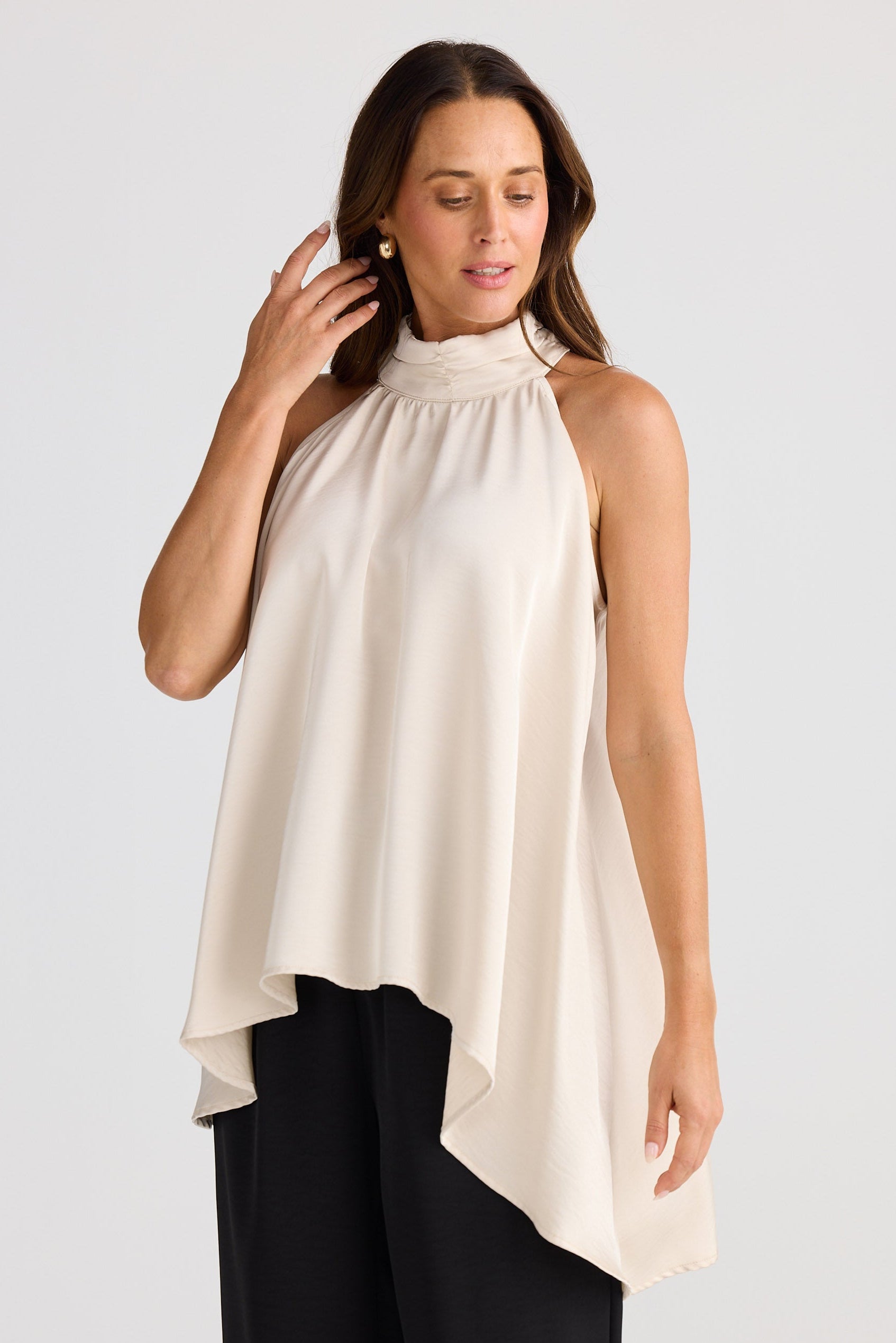 Woman wearing a sleeveless cream top with a high neckline against a plain background