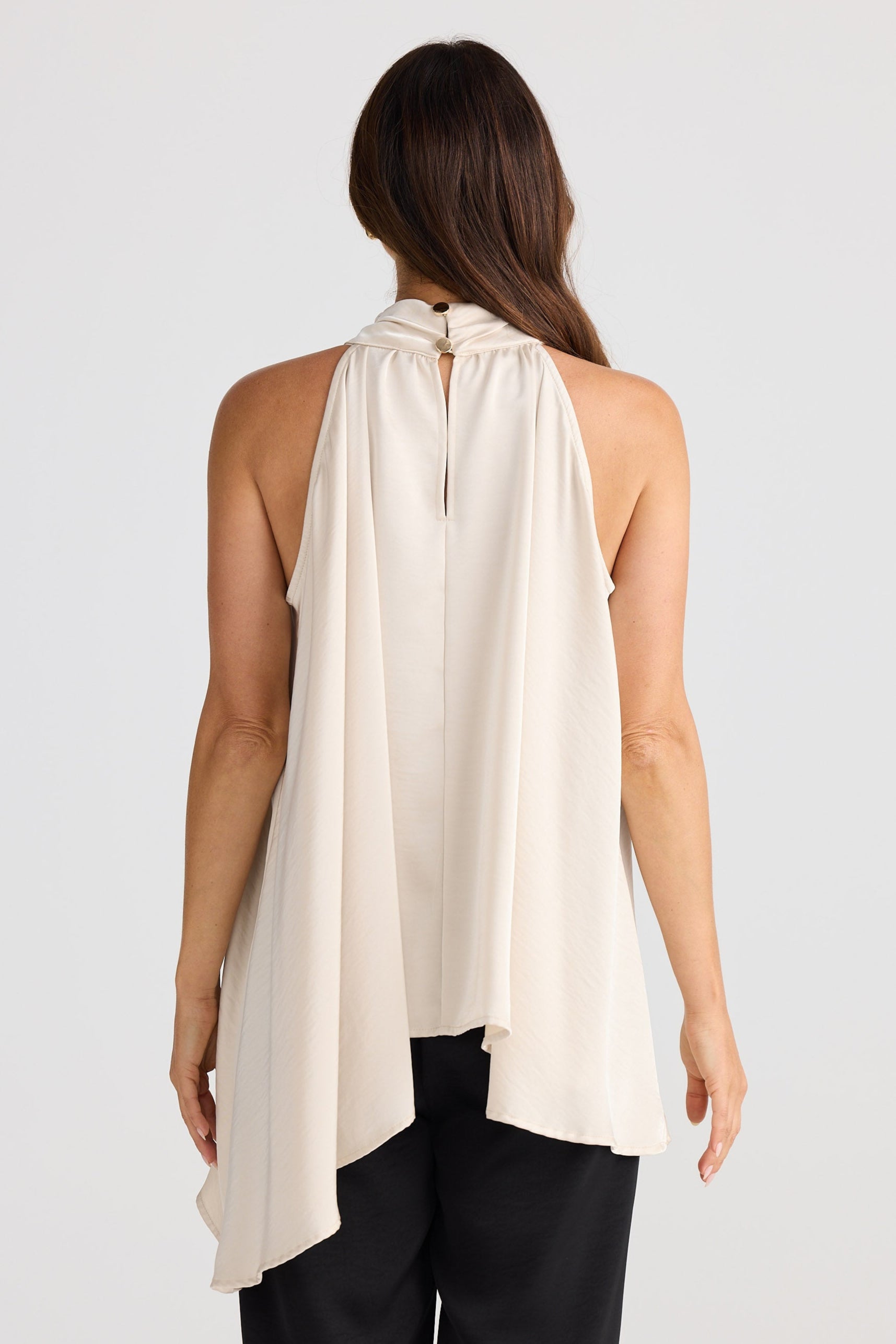 Woman wearing a beige halter top and black pants on a white background