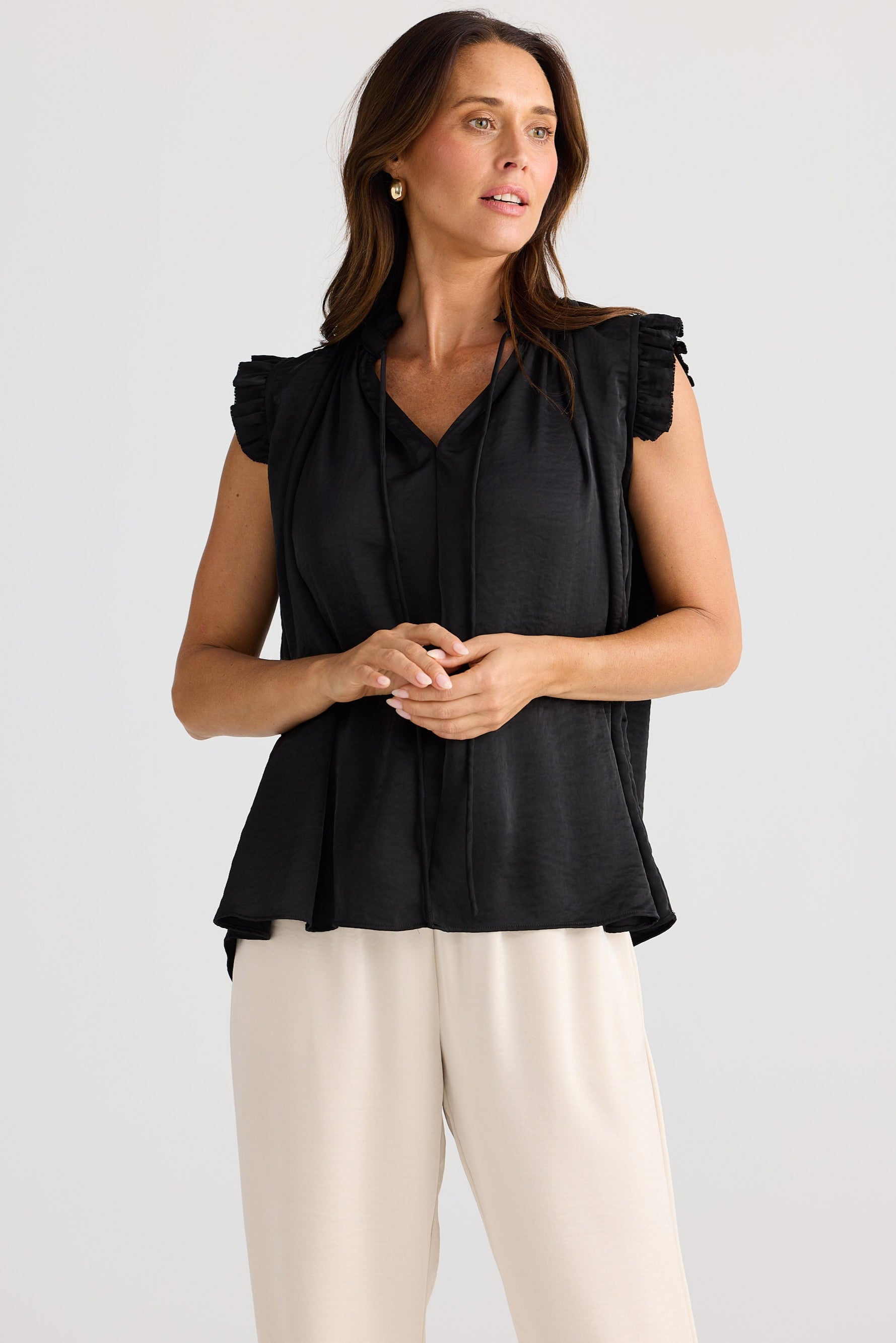 Woman wearing a black sleeveless top with ruffled shoulders against a white background