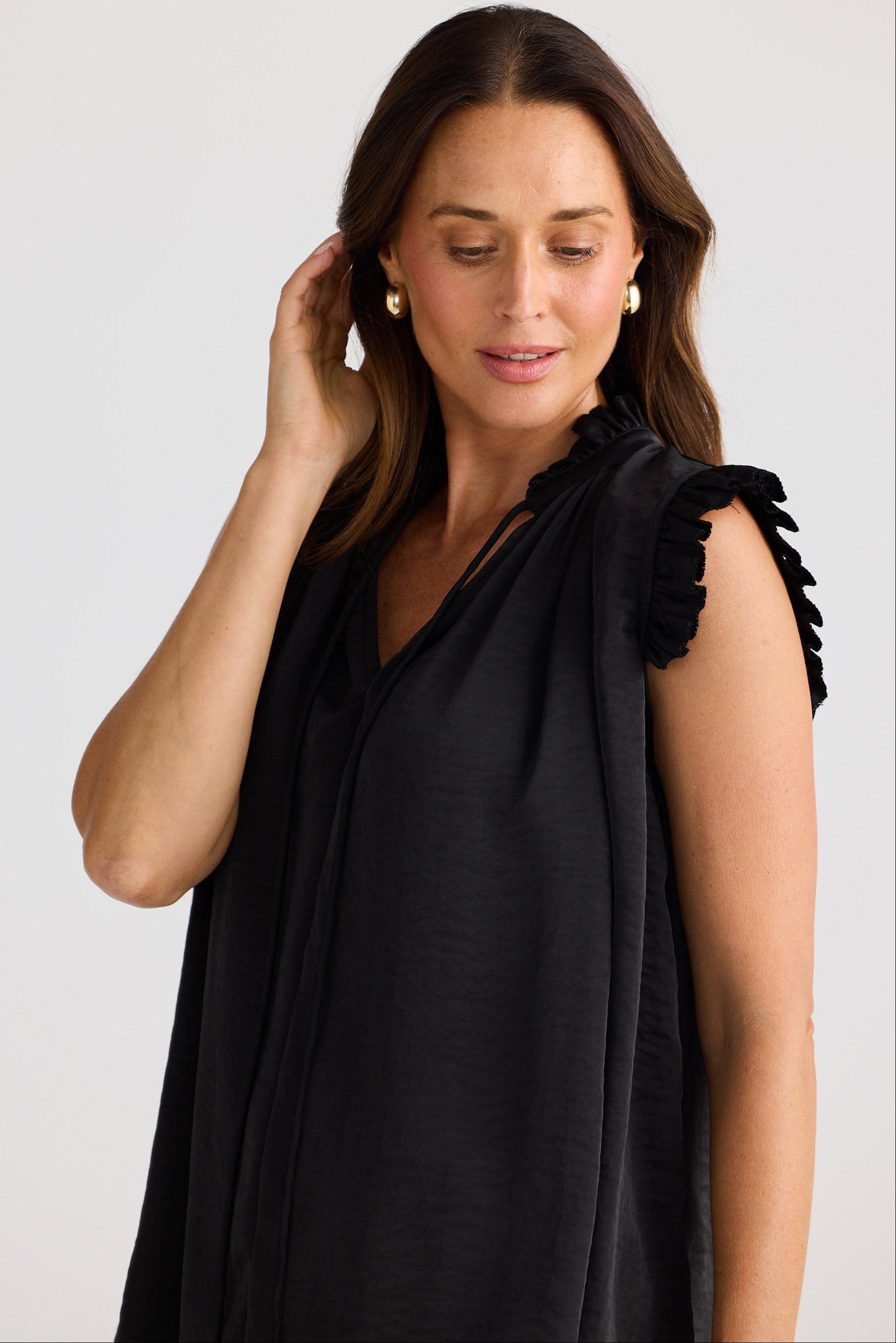 Woman wearing a black dress with ruffled shoulders against a plain background
