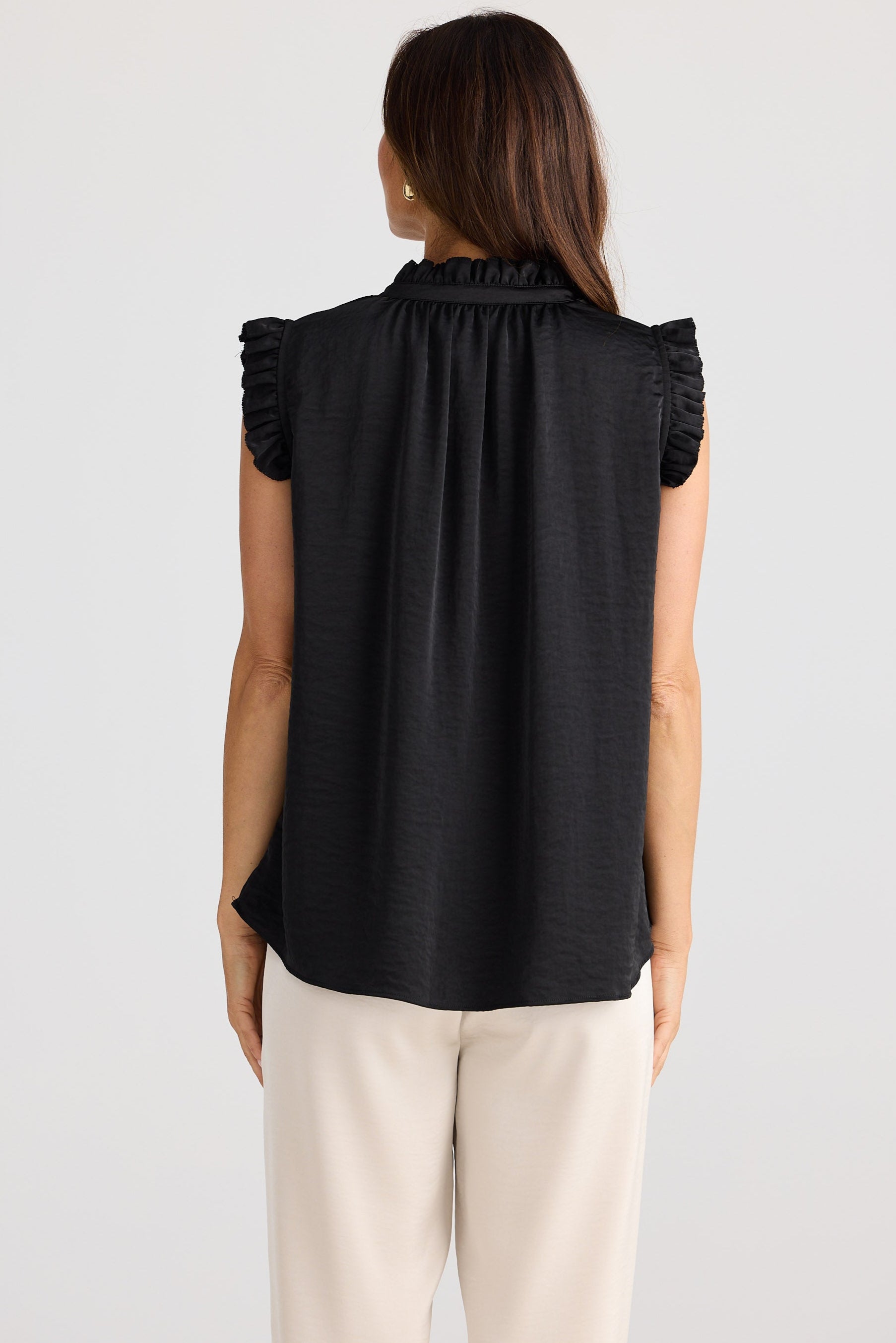 Woman wearing a black sleeveless top with ruffled shoulders on a white background