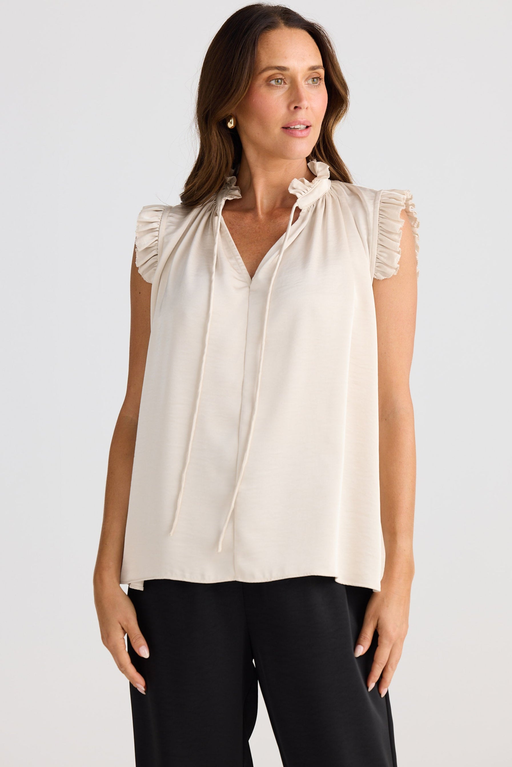 Woman wearing a beige blouse with ruffled shoulders against a white background