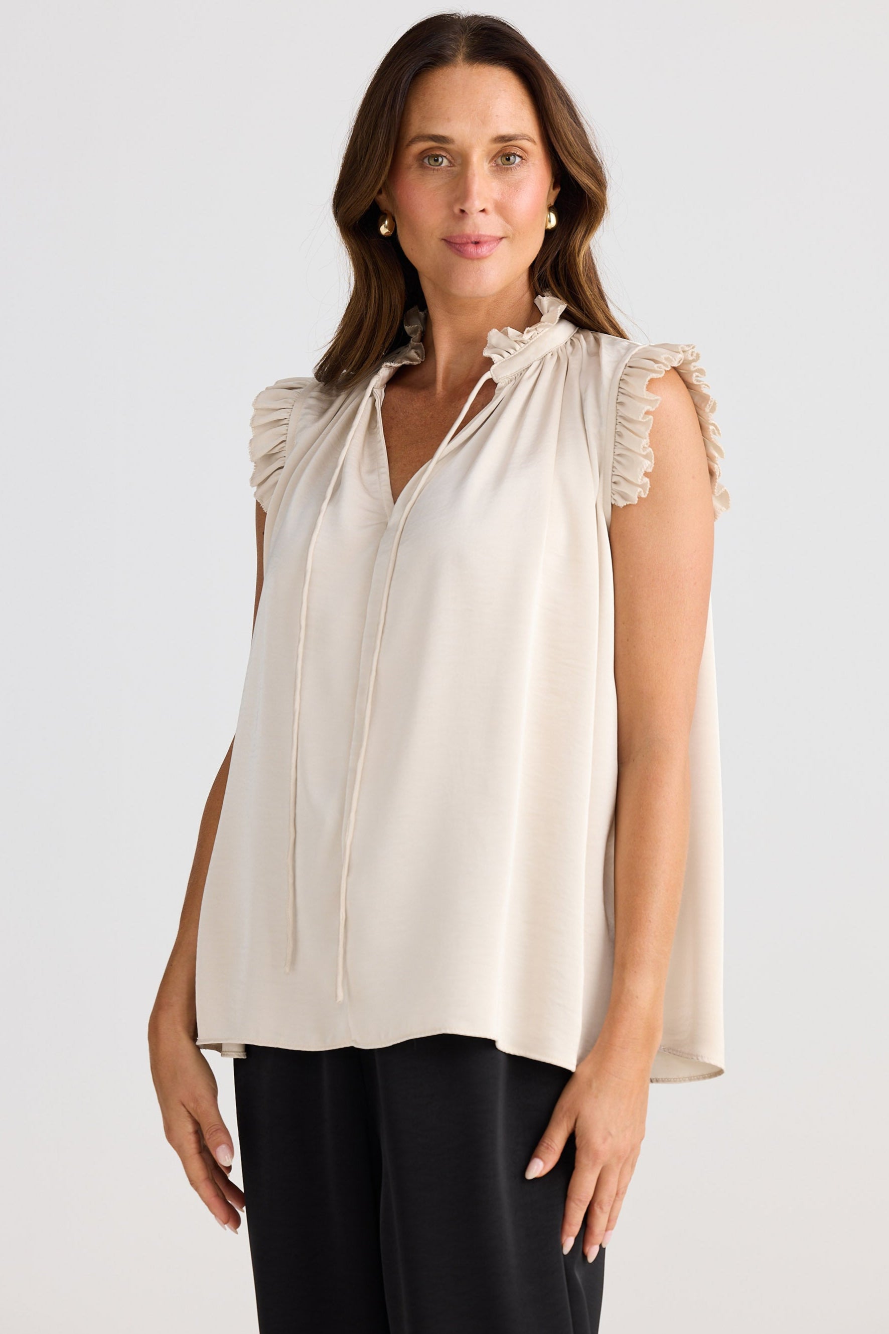 Woman wearing a beige sleeveless blouse with ruffled shoulders against a white background