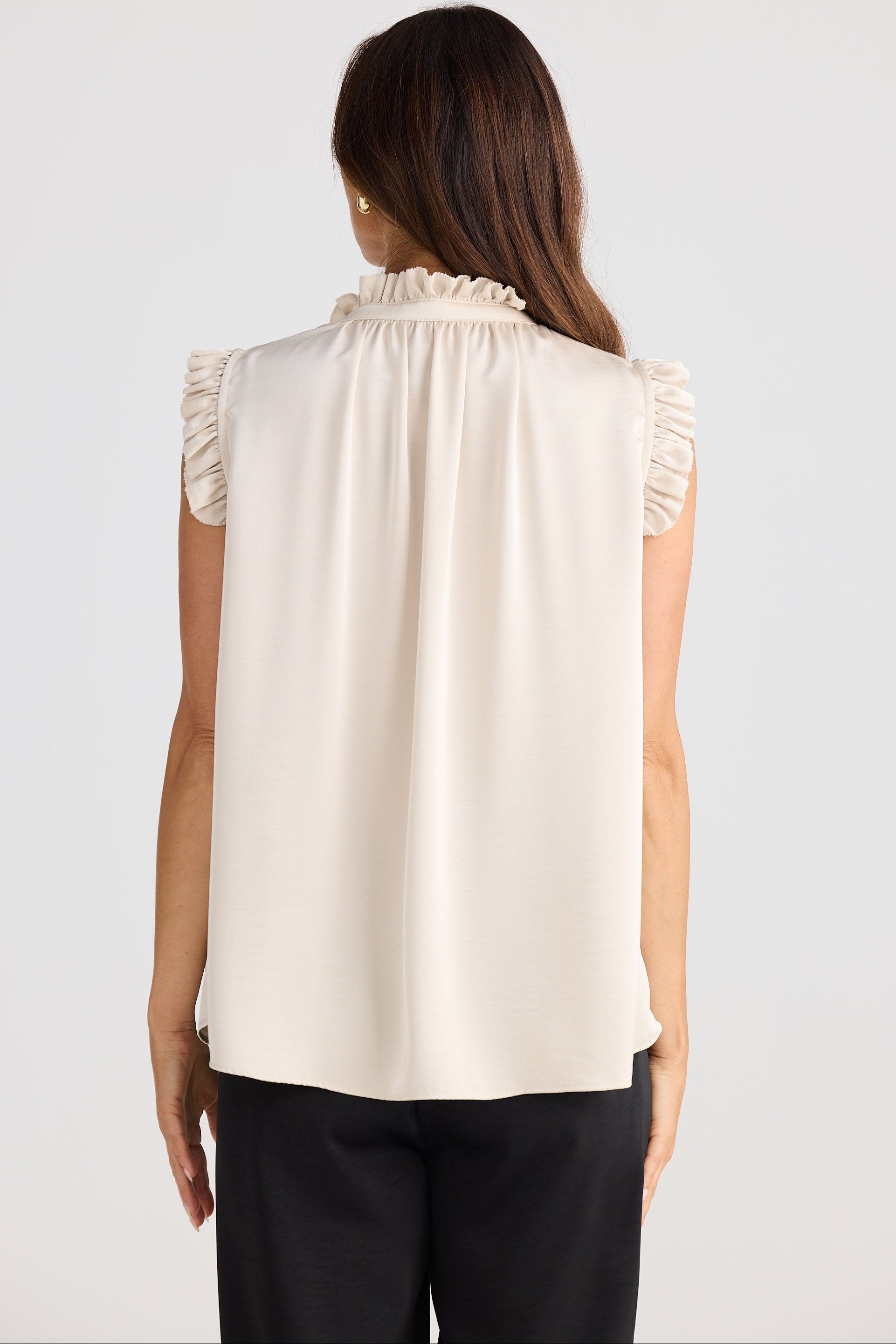 Woman wearing a beige sleeveless blouse with ruffled details on a white background