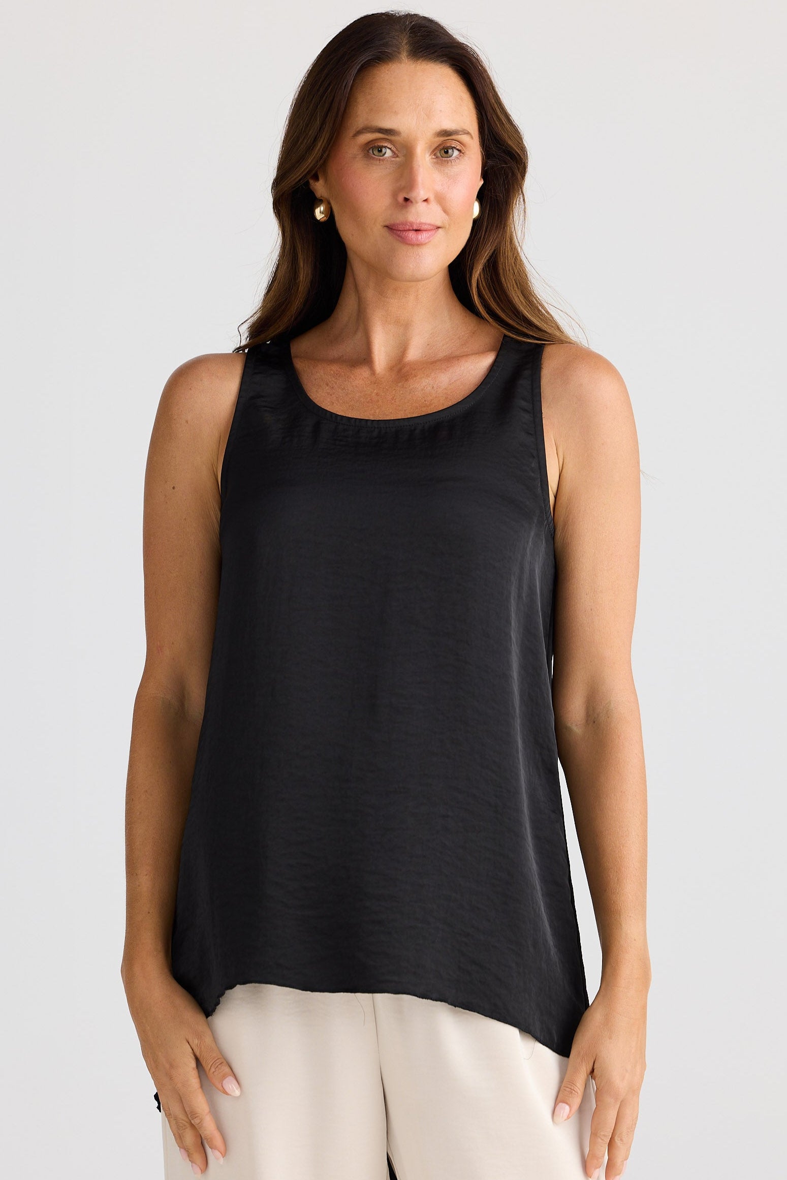Woman wearing a black satin tank top with cream pants.