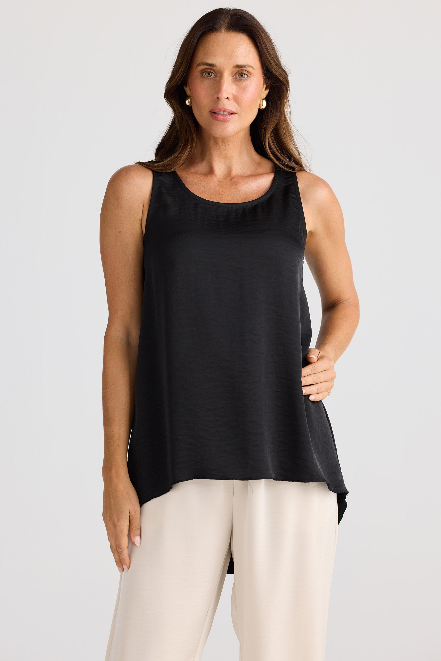 Woman wearing a black satin tank top with cream pants.