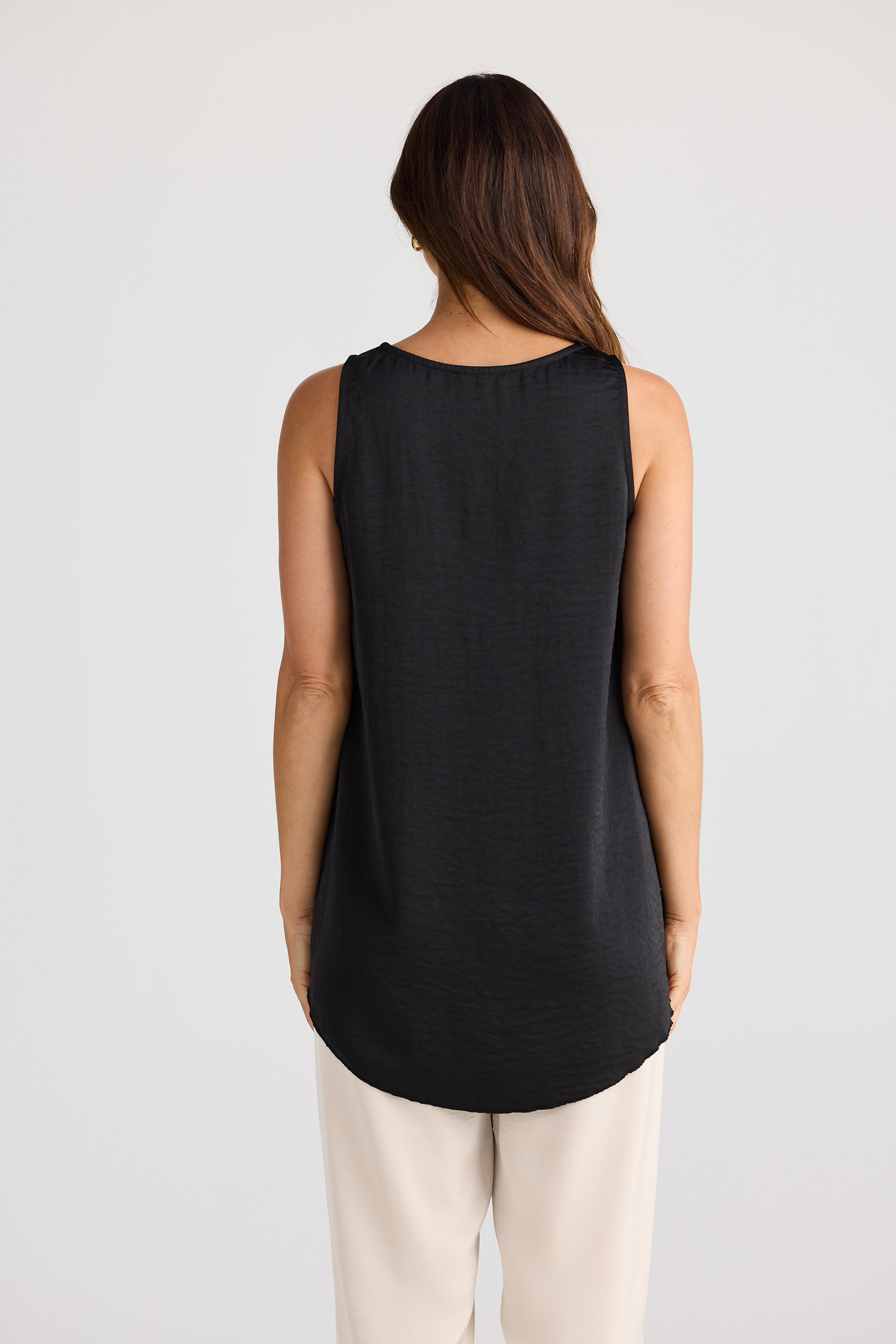 Woman wearing a black satin tank top with cream pants.