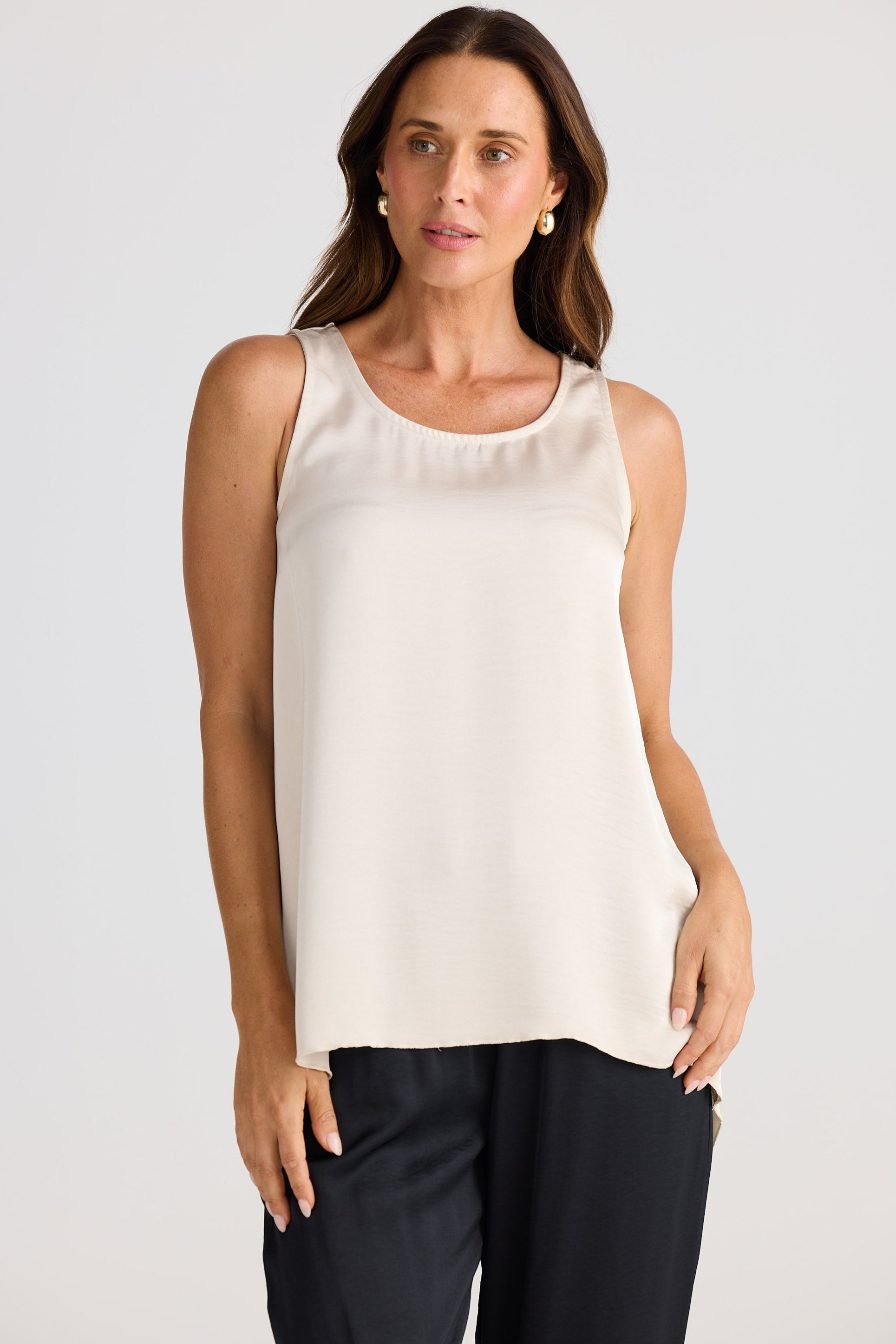 Woman wearing a beige sleeveless top and black pants against a plain background