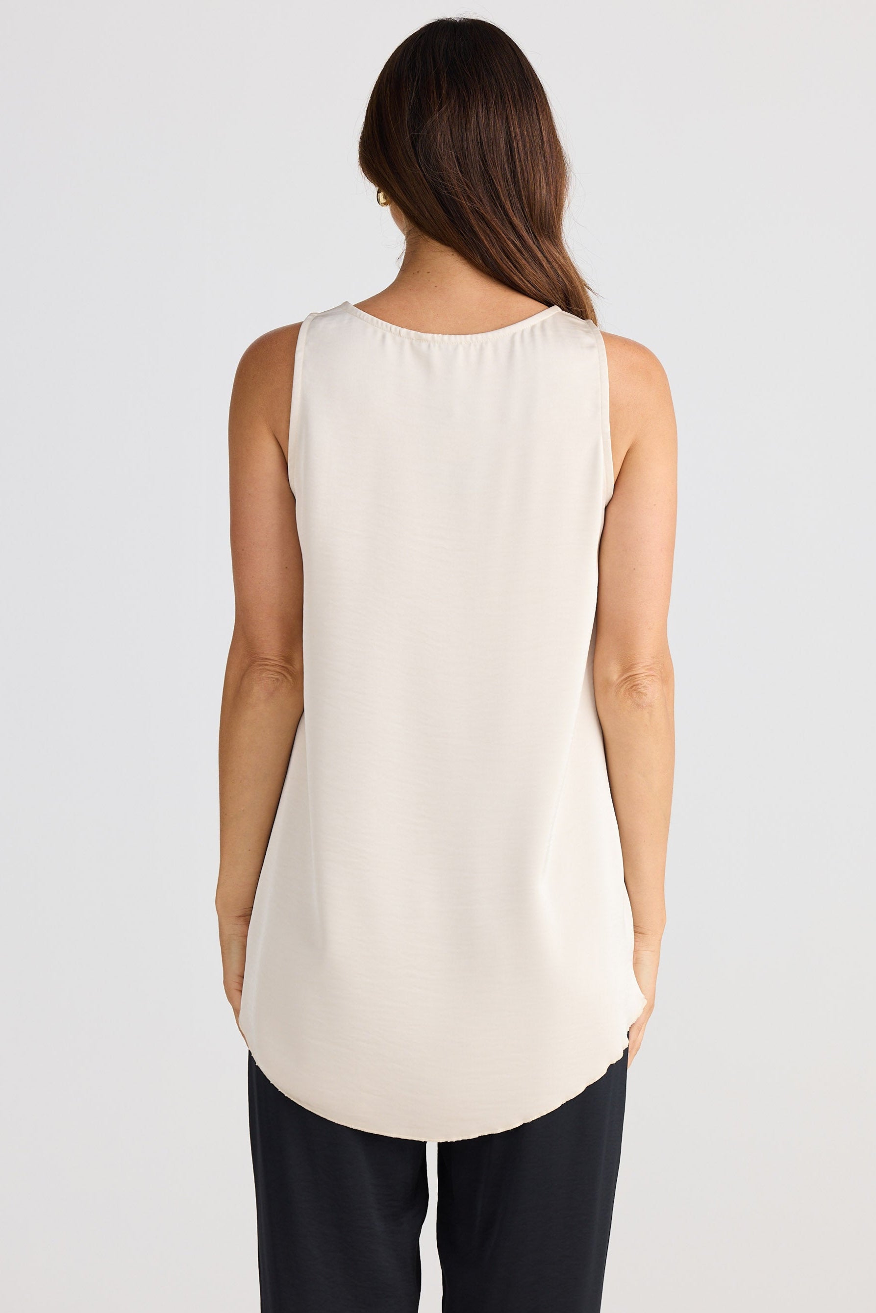Woman wearing a sleeveless beige top and black pants on a white background