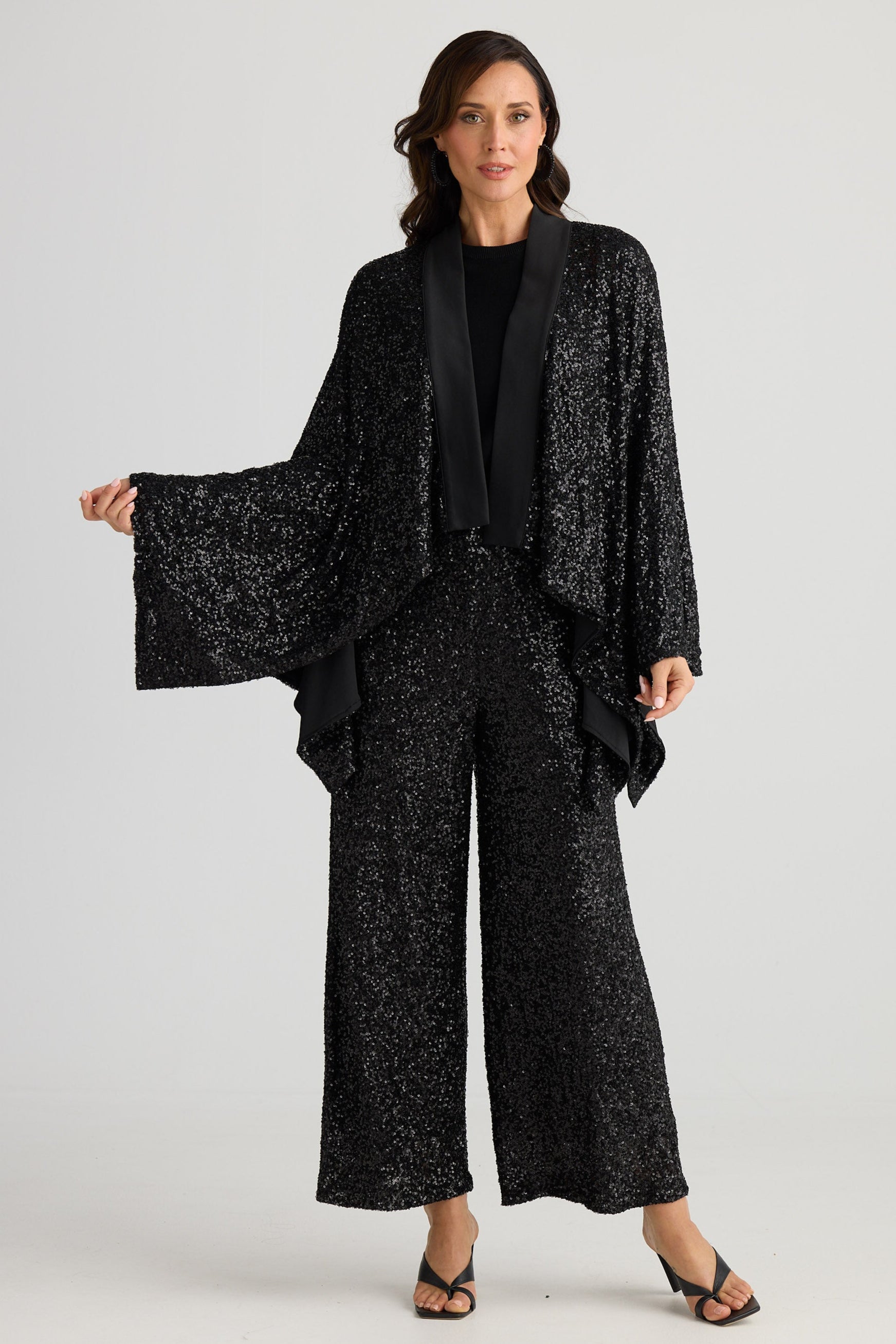 Woman wearing a black textured outfit with wide-leg pants on a white background