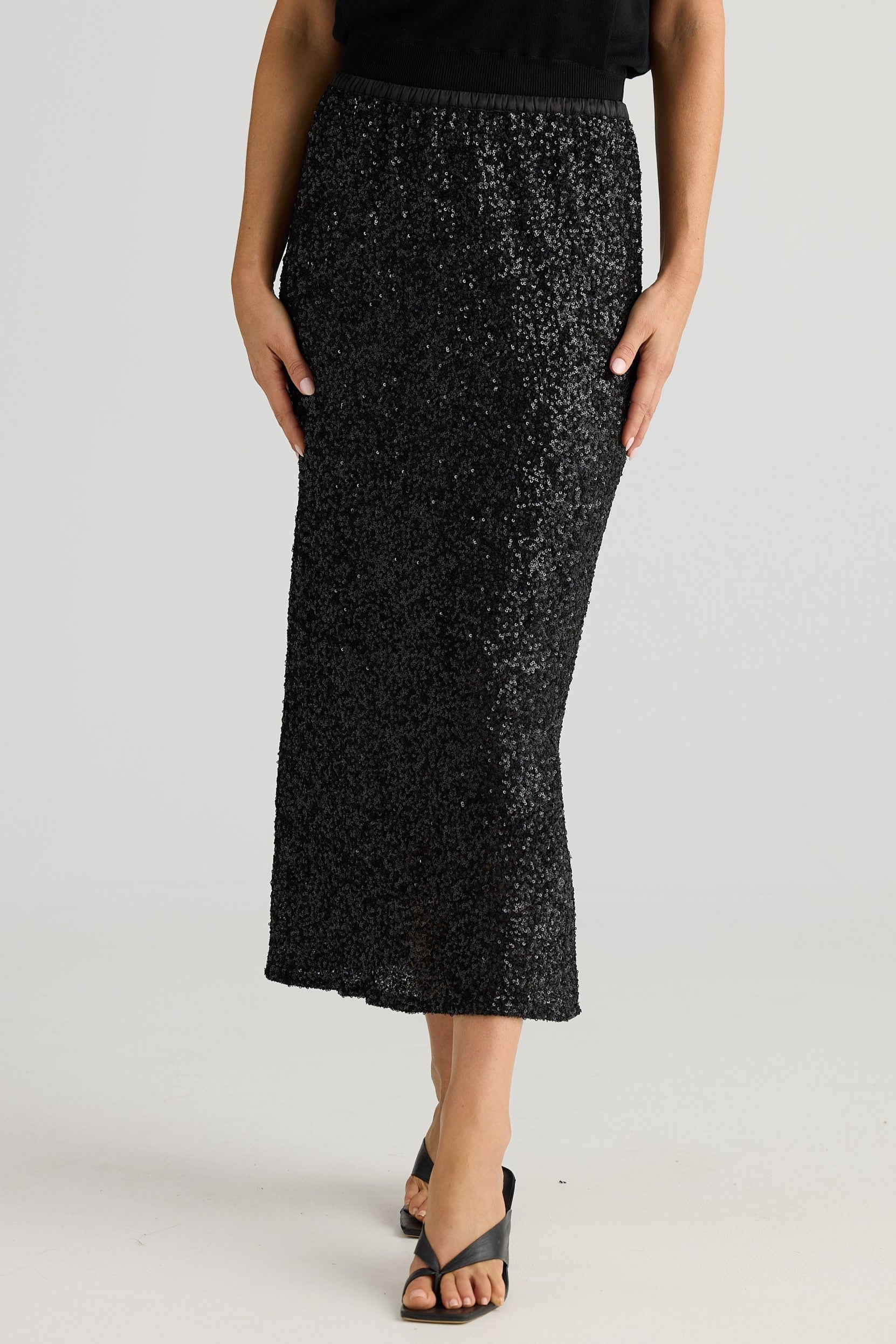 Person wearing a black sequin skirt on a plain background