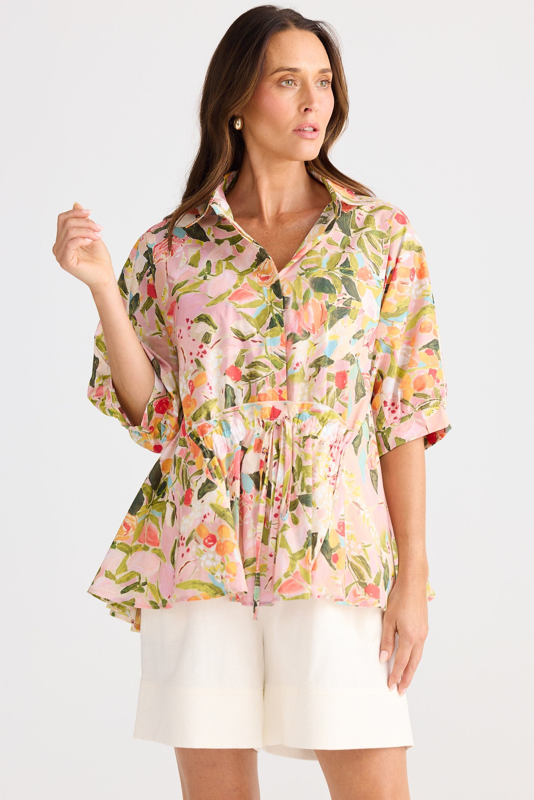 Woman wearing a floral blouse and white shorts on a plain background