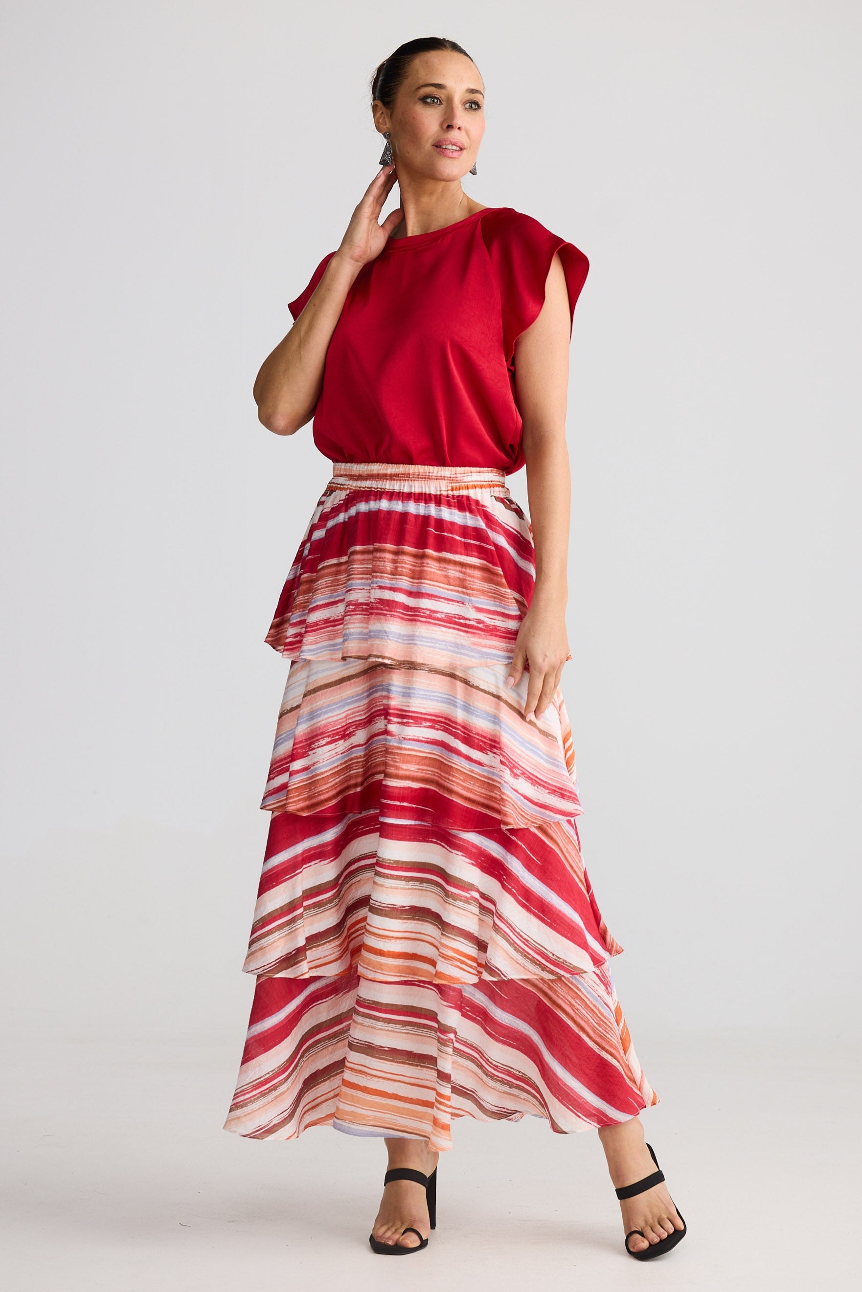 Woman wearing a red top and a long, multicolored striped skirt on a white background