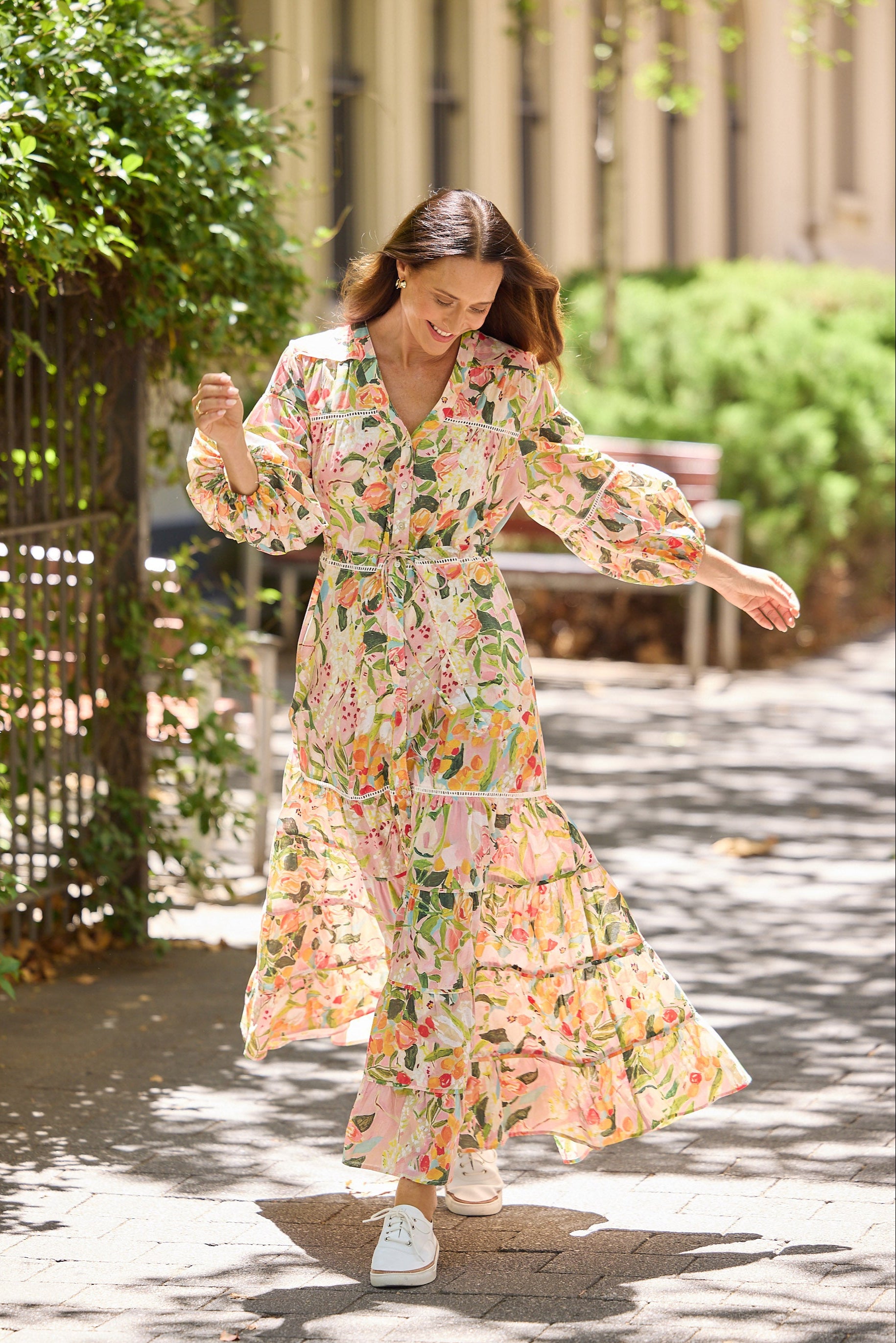 Woman in a floral dress standing on a tree-shadowed path