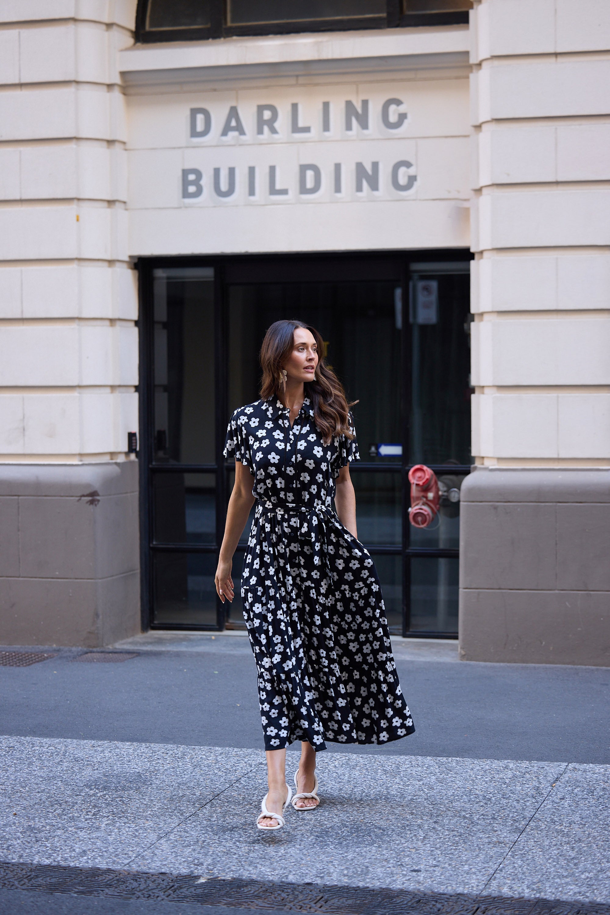 Woman in a black floral dress standing in front of a building with 'Darling Building' signage.