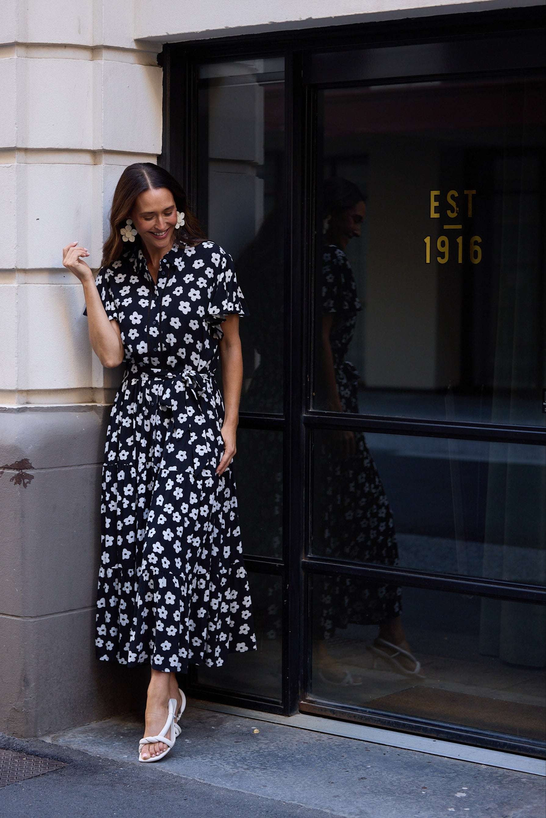 Woman in a black floral dress standing outside a building with a glass door.