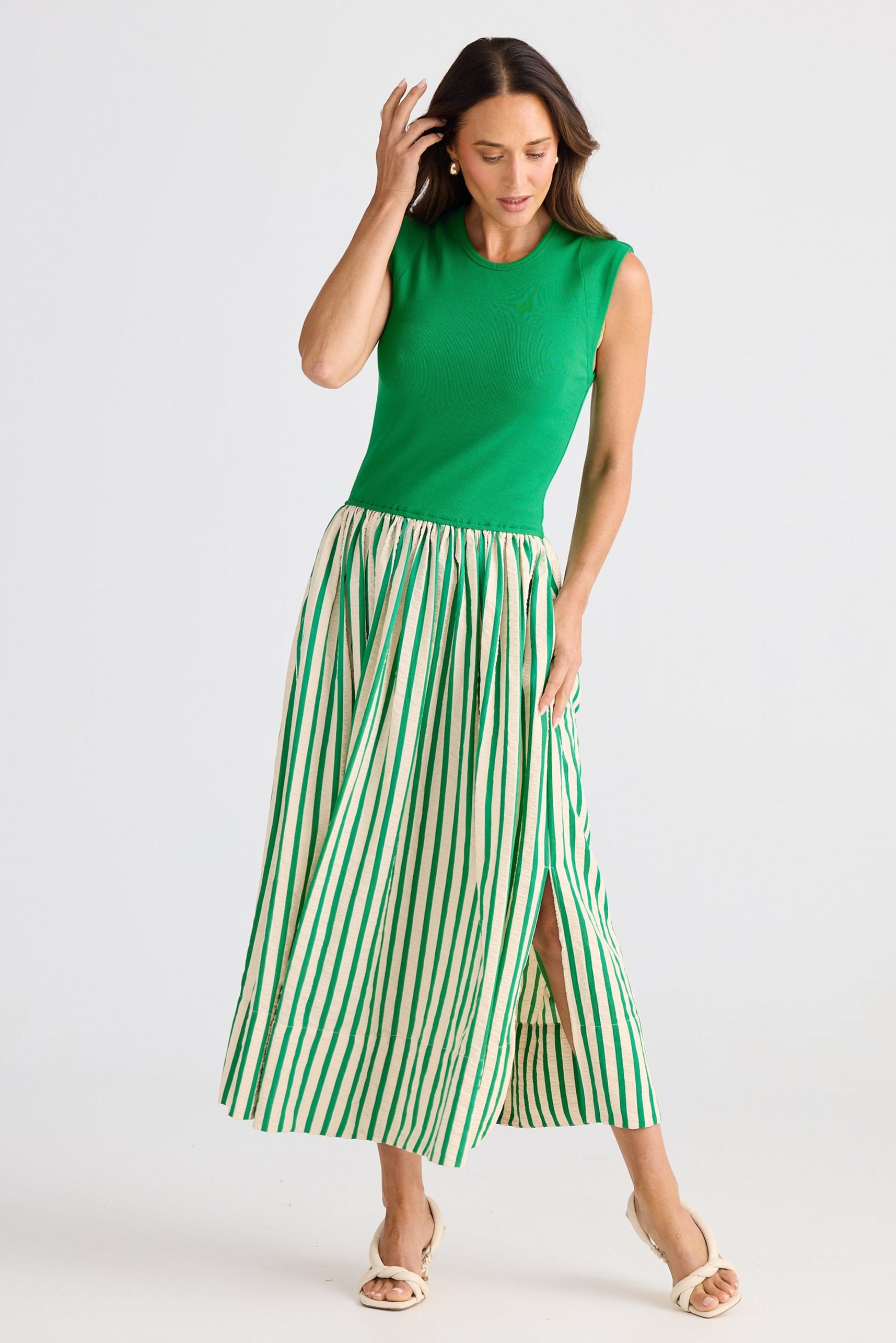 Woman wearing a dress with a green sleeveless top and green and white striped skirt on a white background