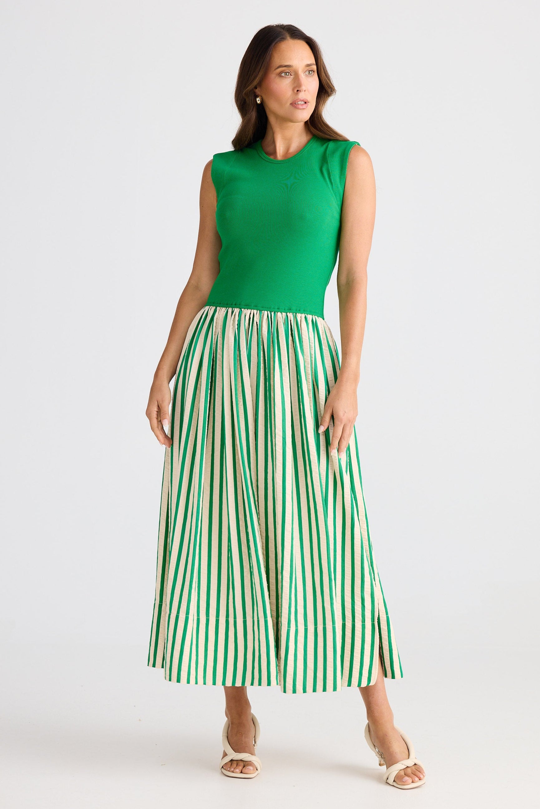 Woman wearing a dress with a green sleeveless top and striped skirt on a white background