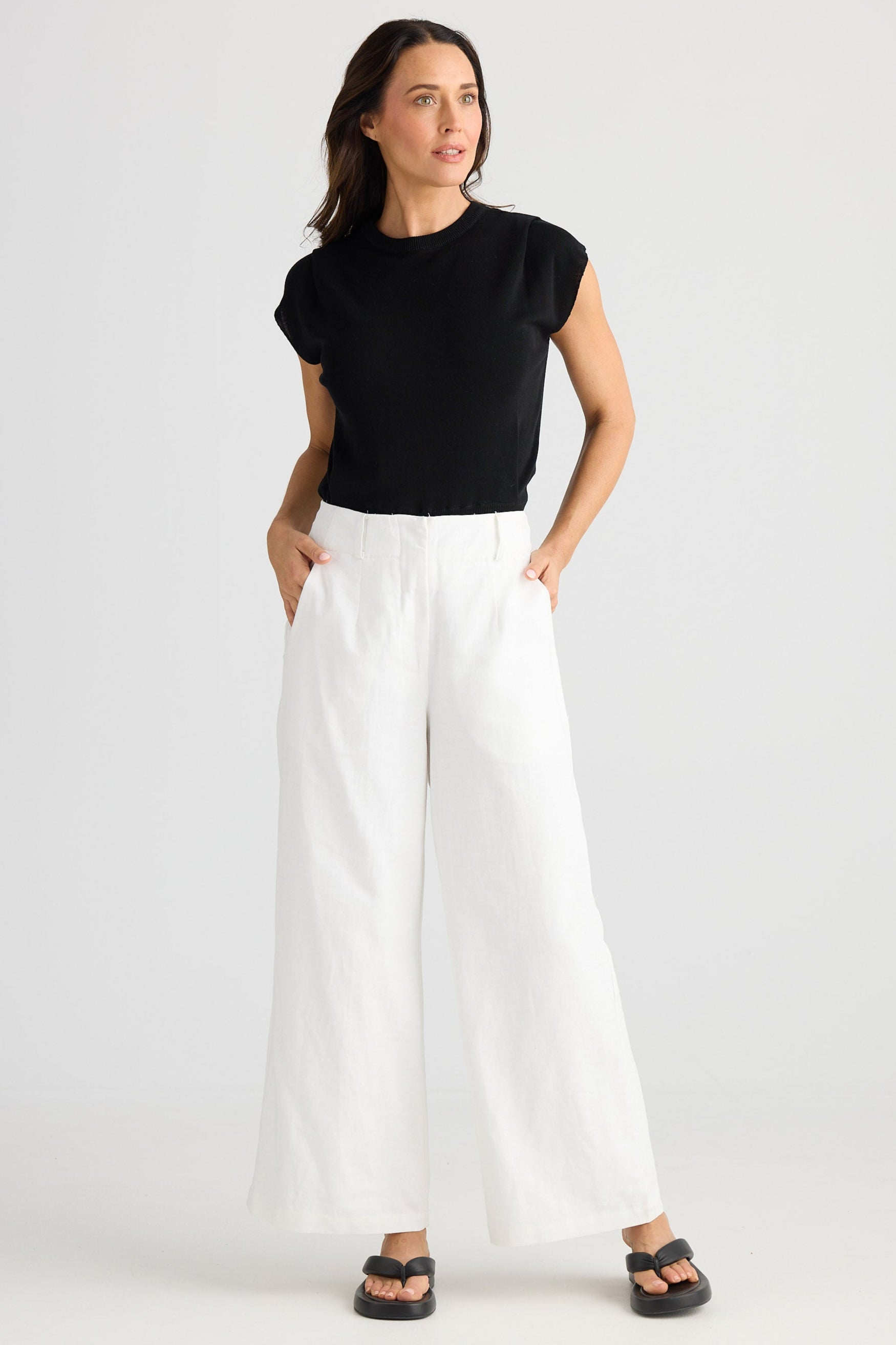 Woman wearing a black top and white pants on a white background
