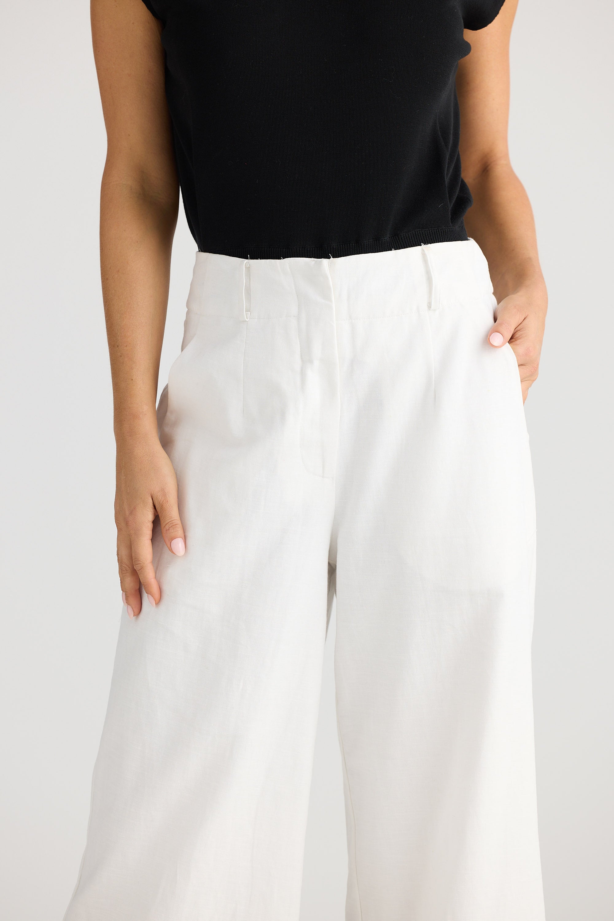 Person wearing a black top and white pants on a plain background