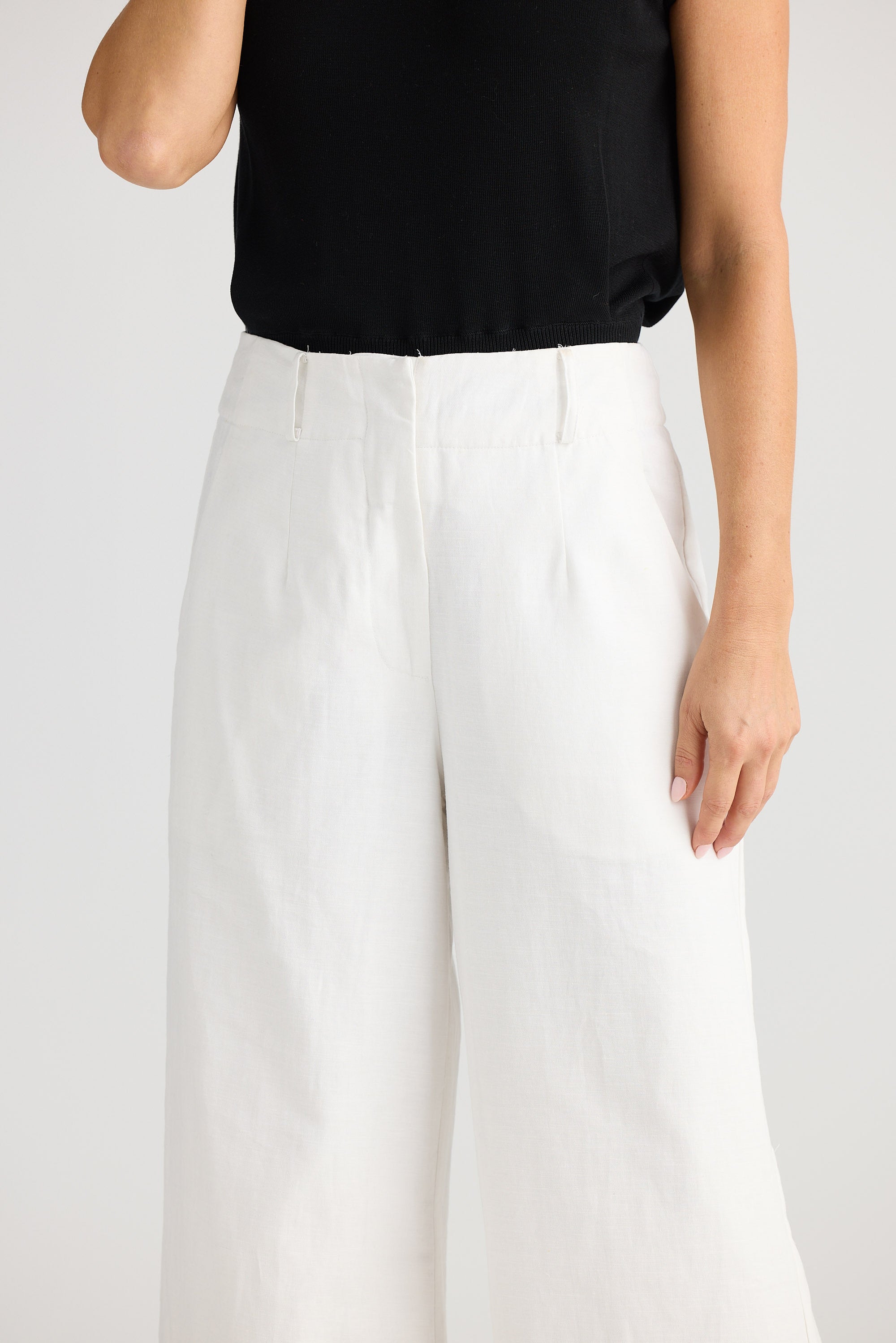 Person wearing white pants and a black top on a plain background