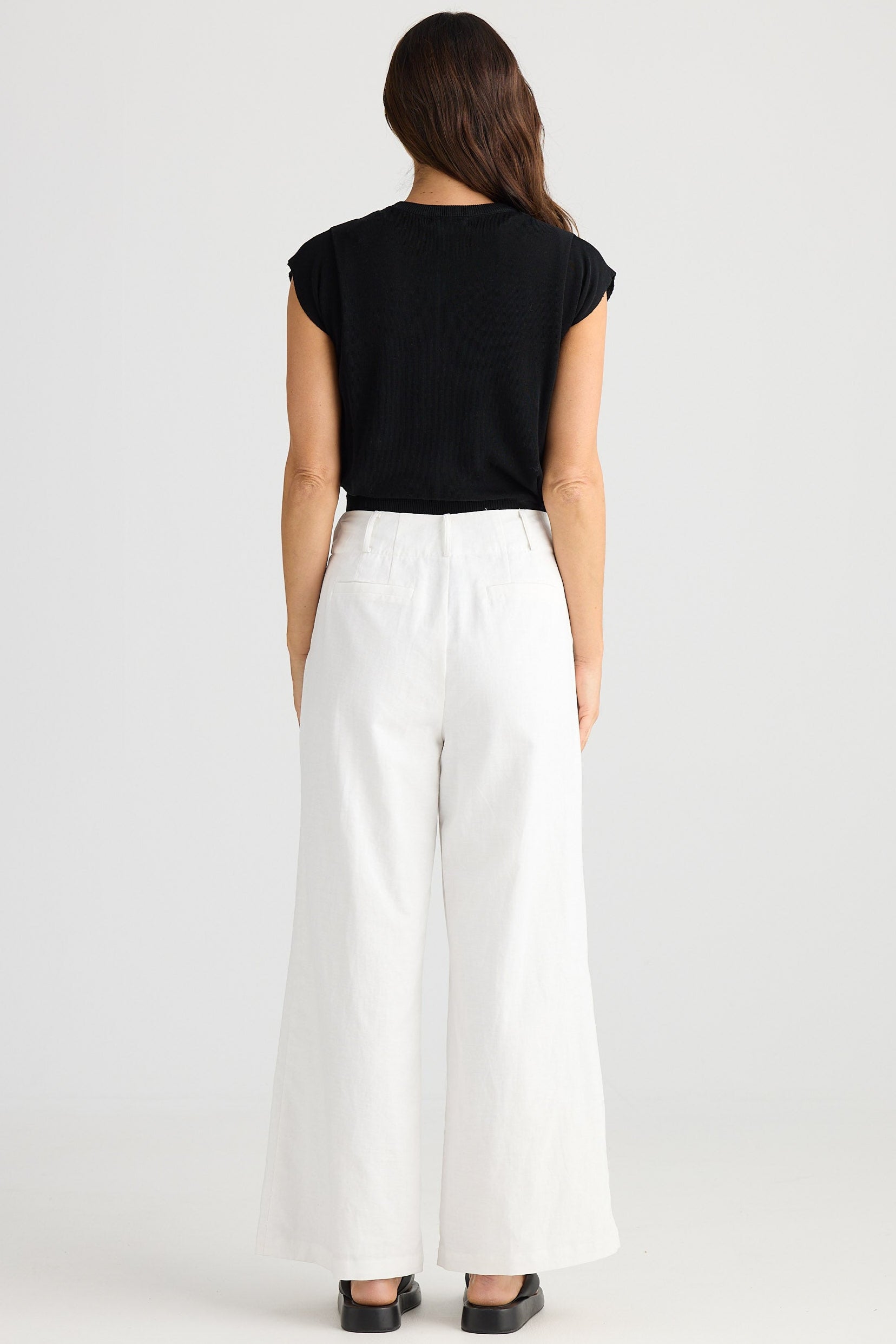 Person wearing a black top and white pants on a white background