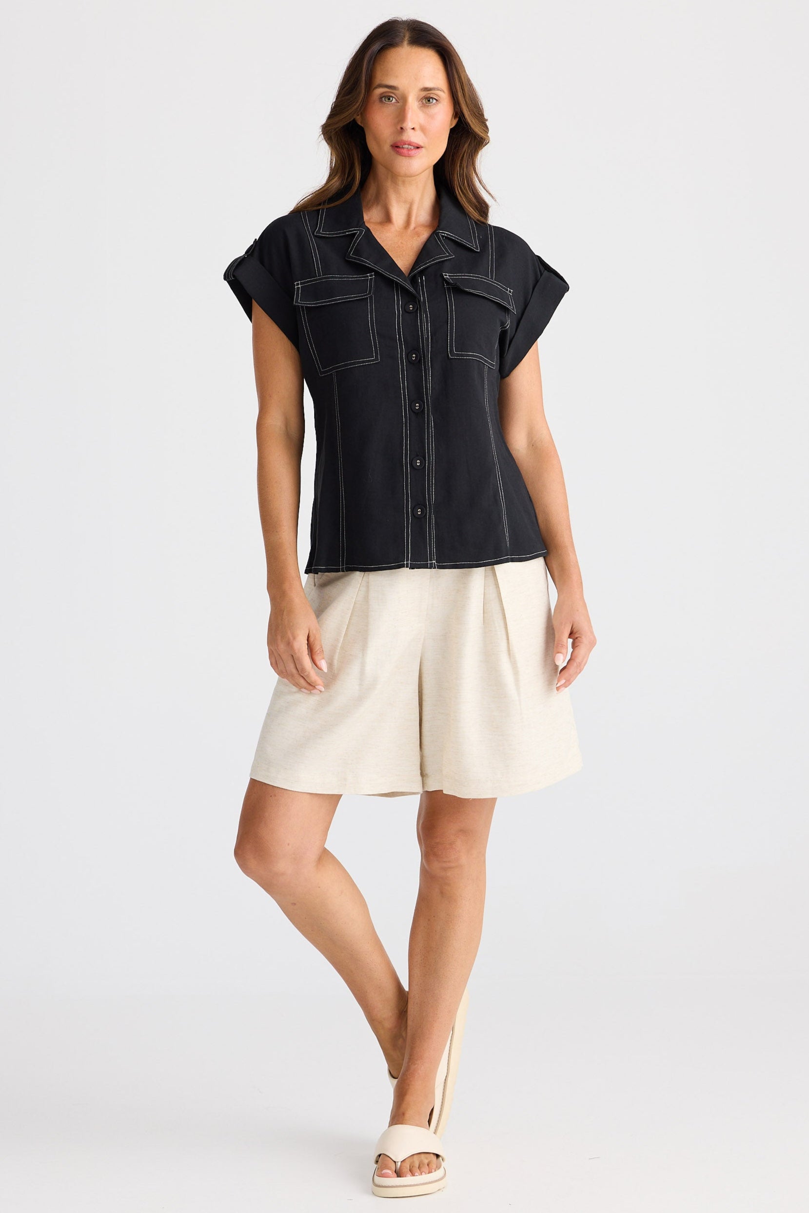 Woman wearing a black cap sleeve shirt and beige shorts on a white background