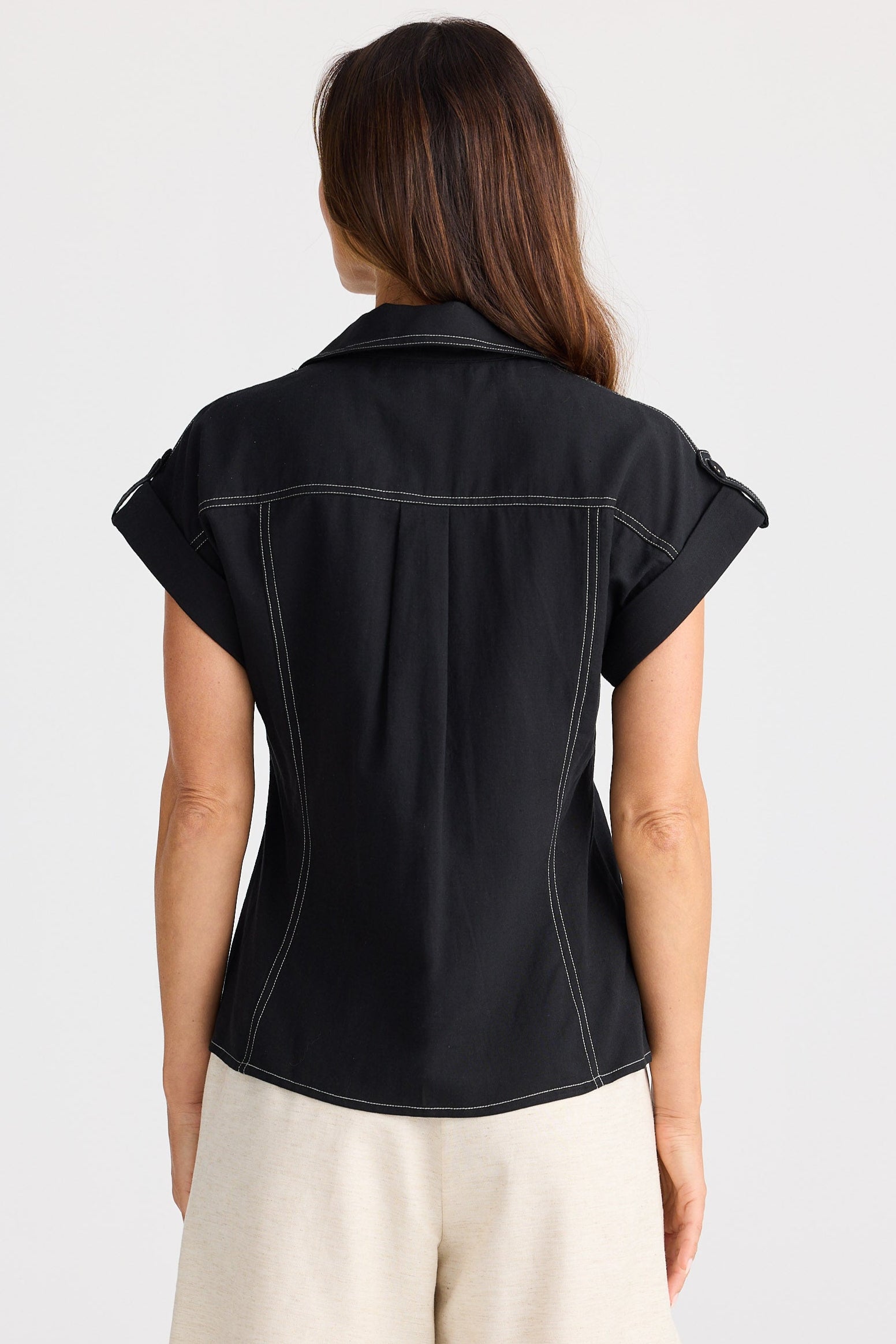 Woman wearing a black sleeveless shirt and beige shorts on a white background