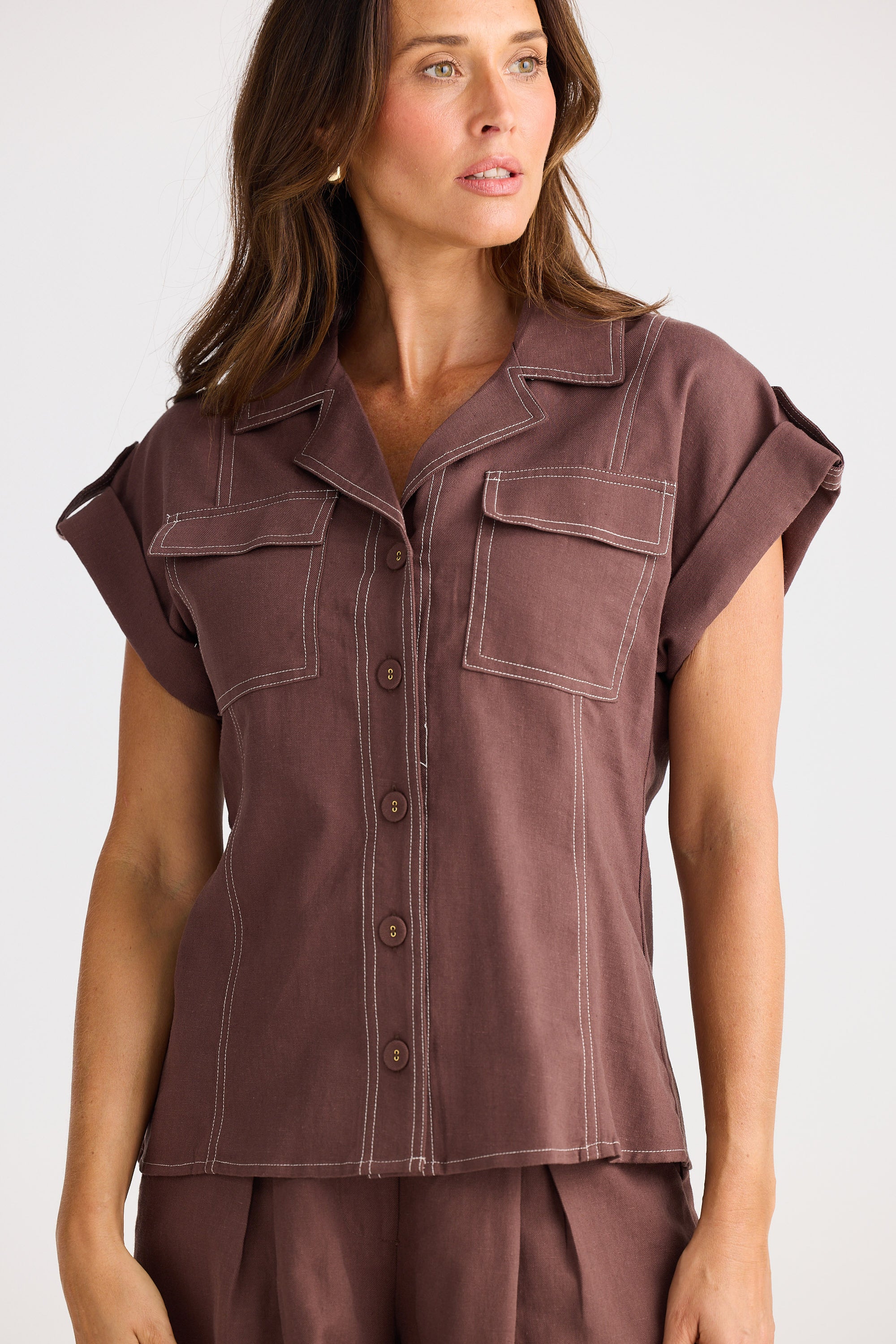 Woman wearing a brown sleeveless shirt with button details on a white background