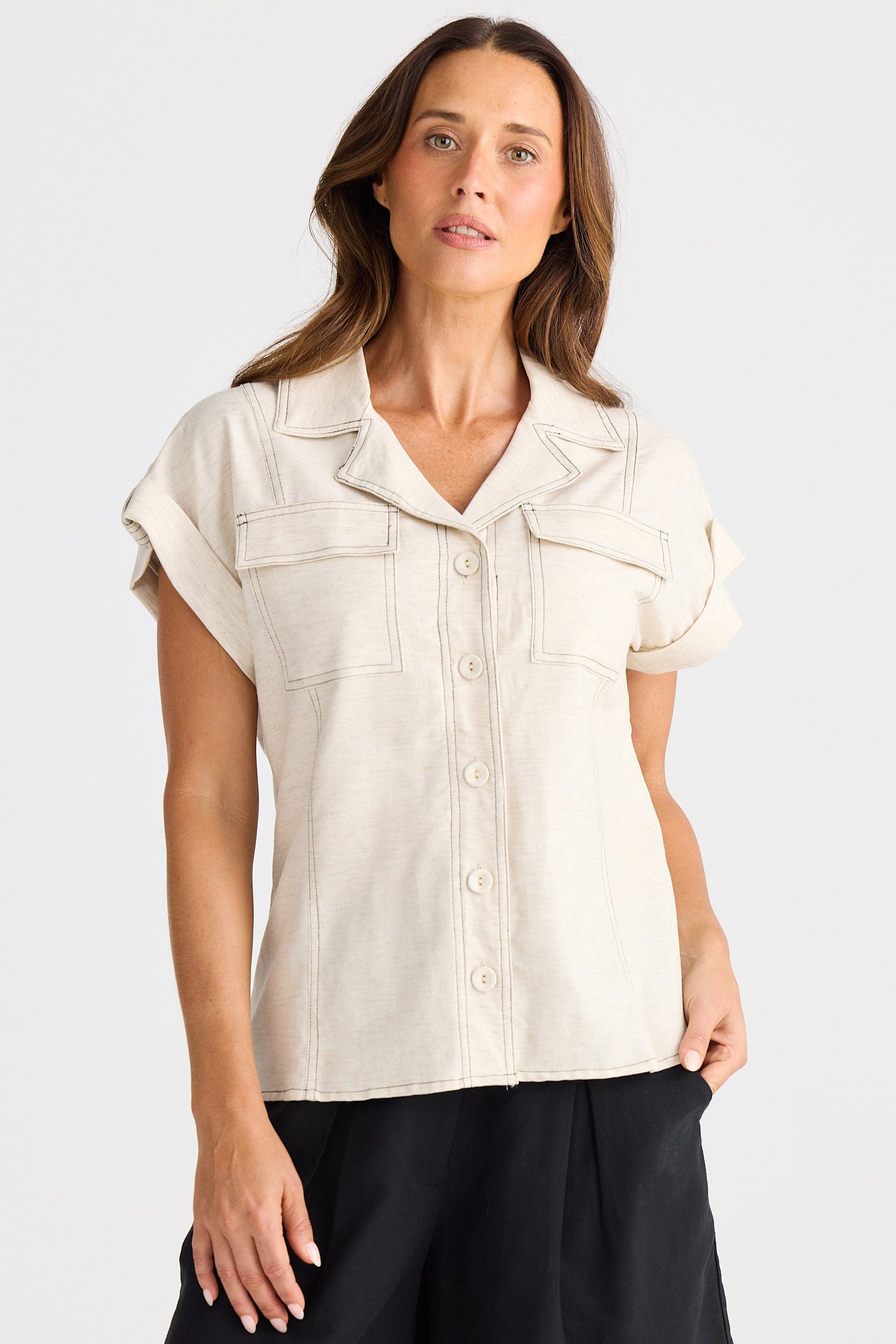 Woman wearing a sleeveless beige top and black shorts on a white background