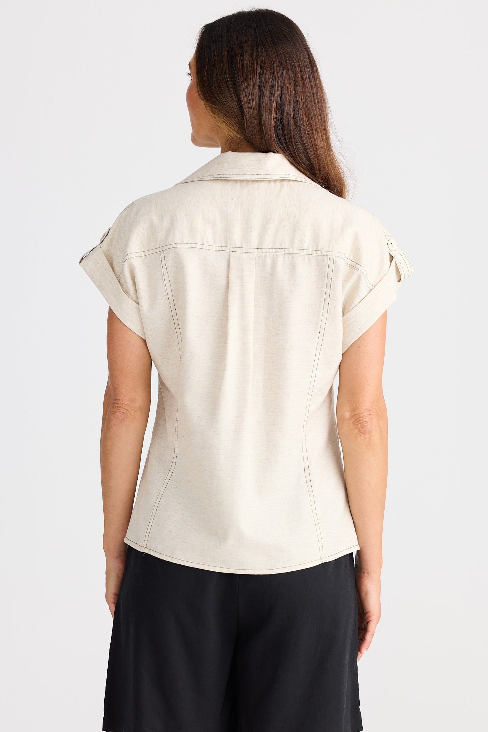Woman wearing a beige sleeveless shirt and black shorts on a white background