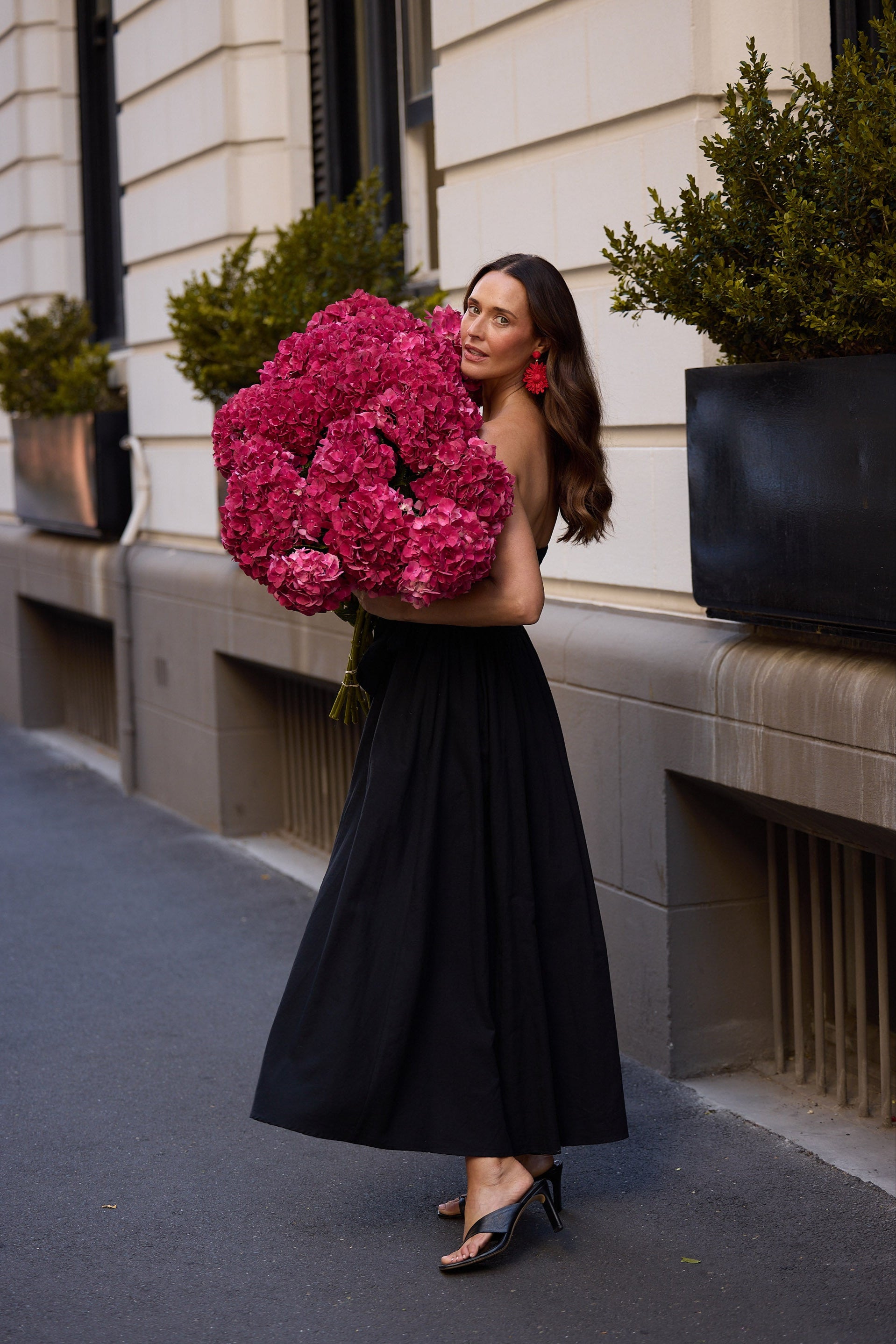 Woman holding a large bouquet of pink flowers in an urban setting.