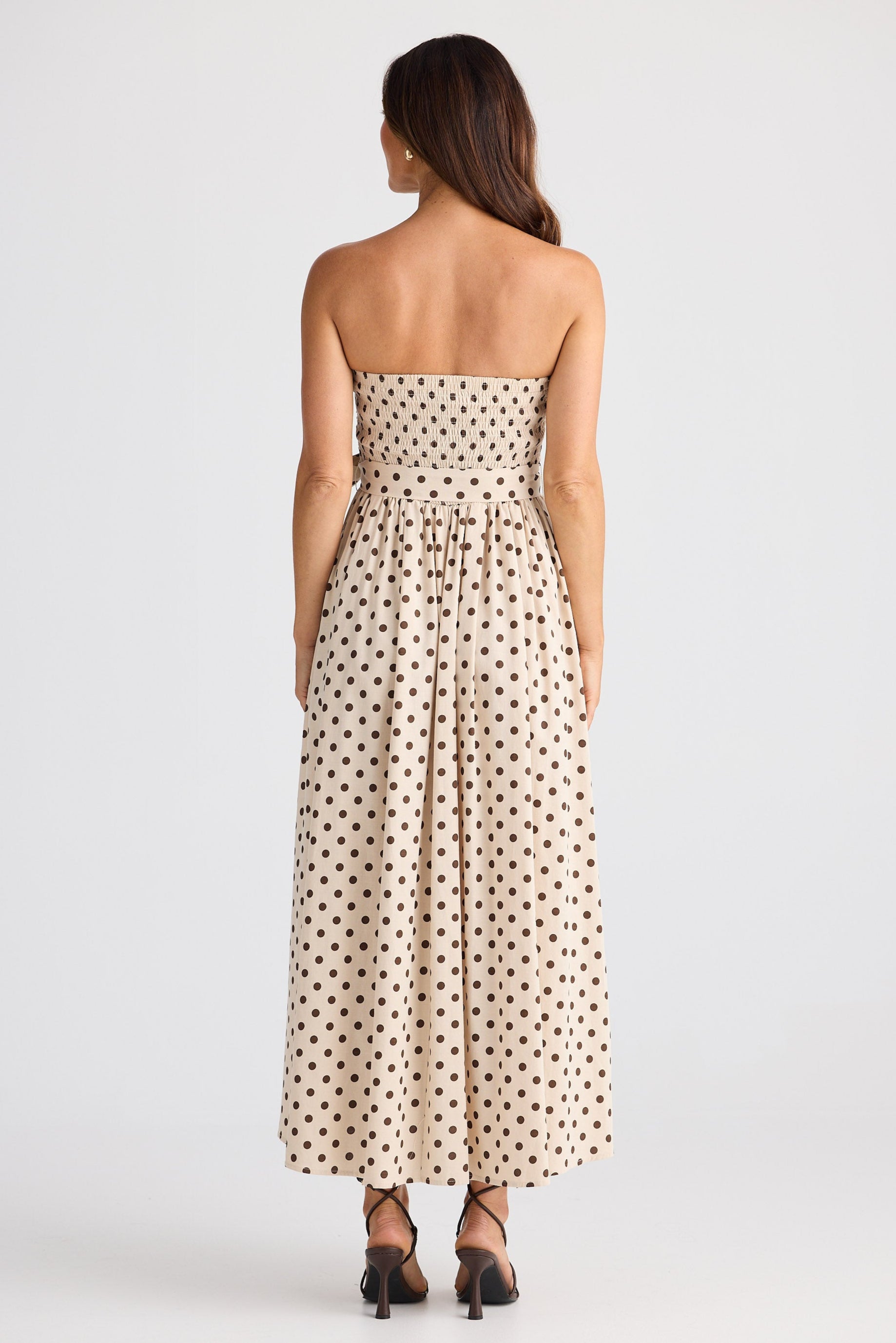 Woman wearing a strapless polka dot dress on a white background