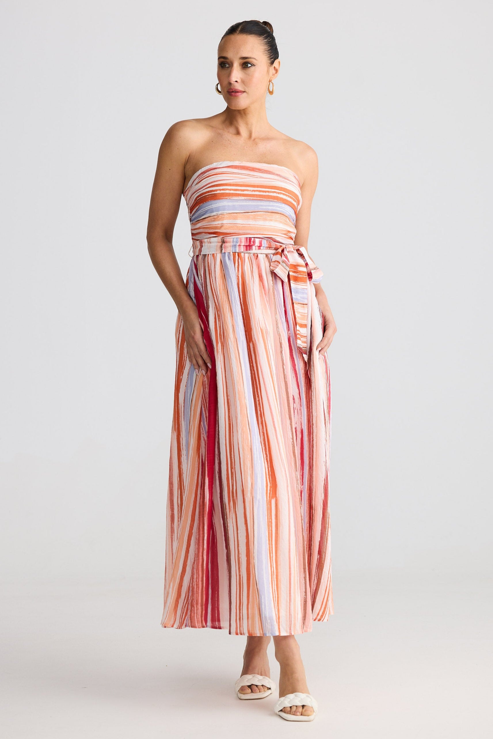 Woman wearing a strapless, multicolored striped dress on a plain background