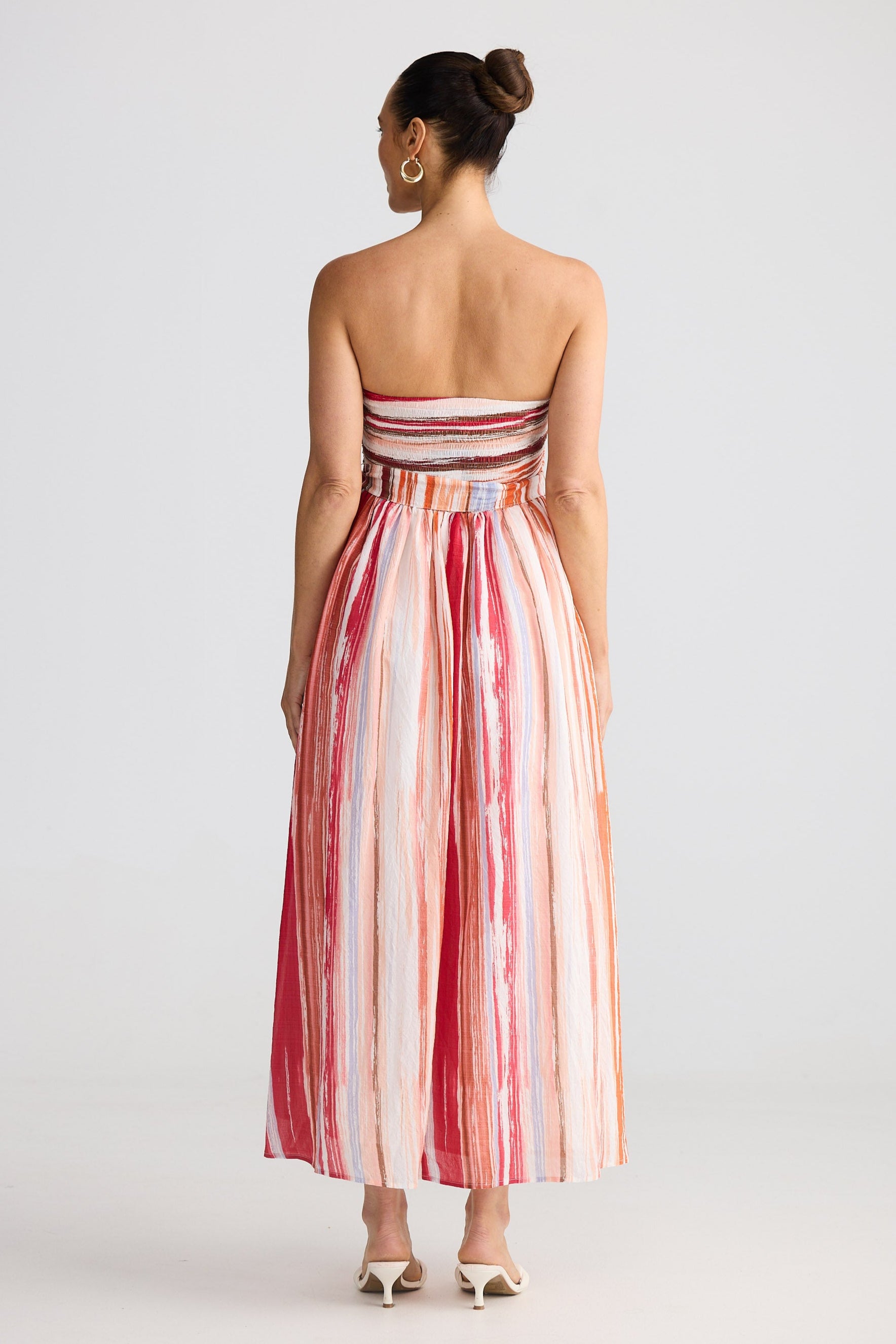 Woman wearing a strapless, long, red and white striped dress on a plain background