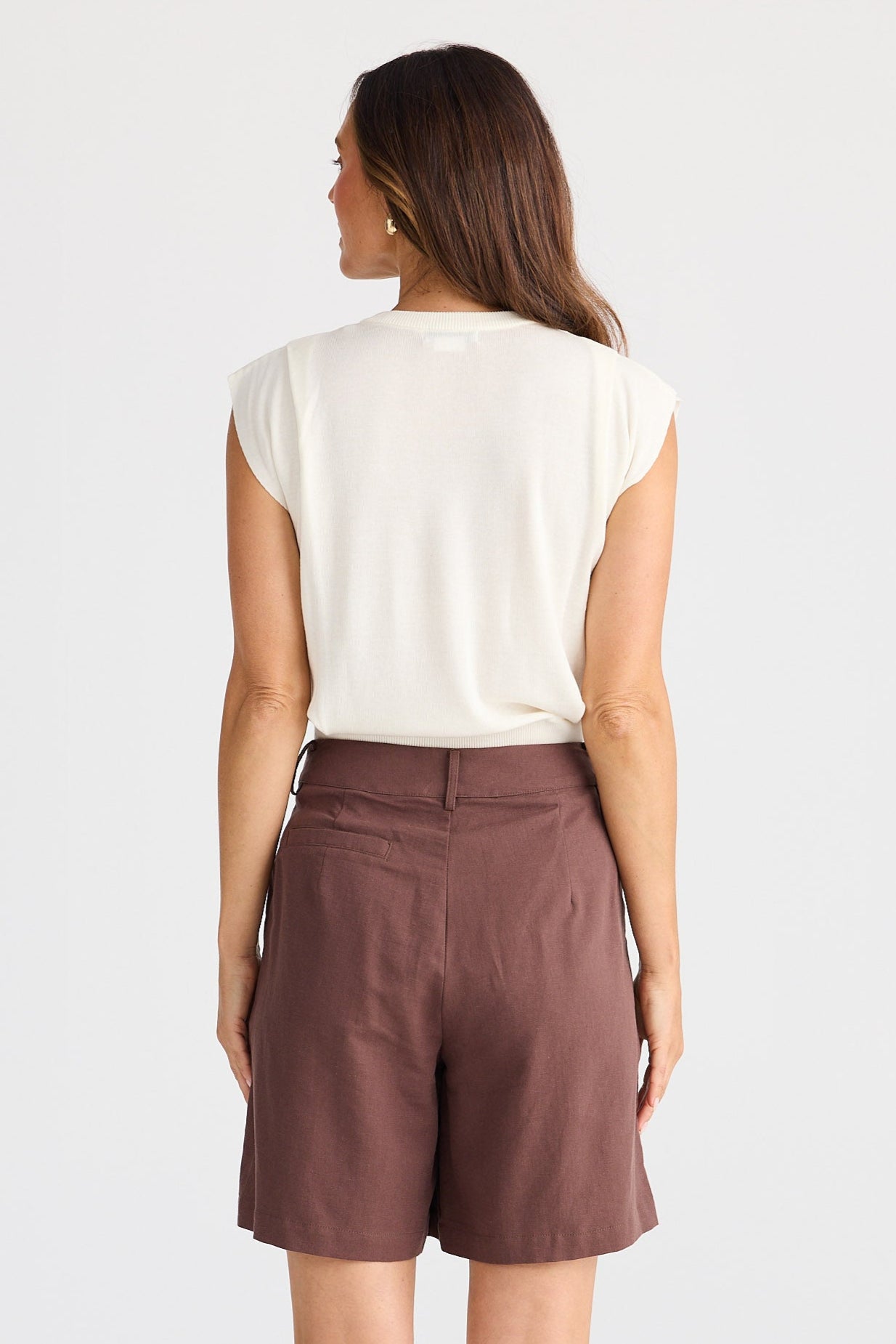 Woman wearing brown shorts and a white top on a plain background