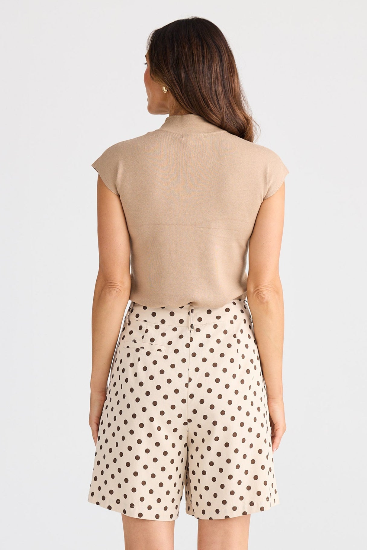 Woman wearing a beige sleeveless top and polka dot shorts on a white background