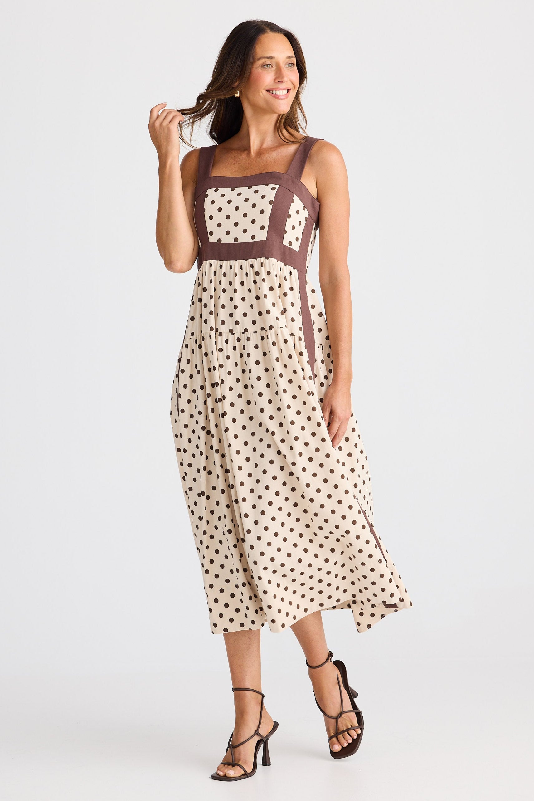 Woman wearing a polka dot dress with a brown top on a white background