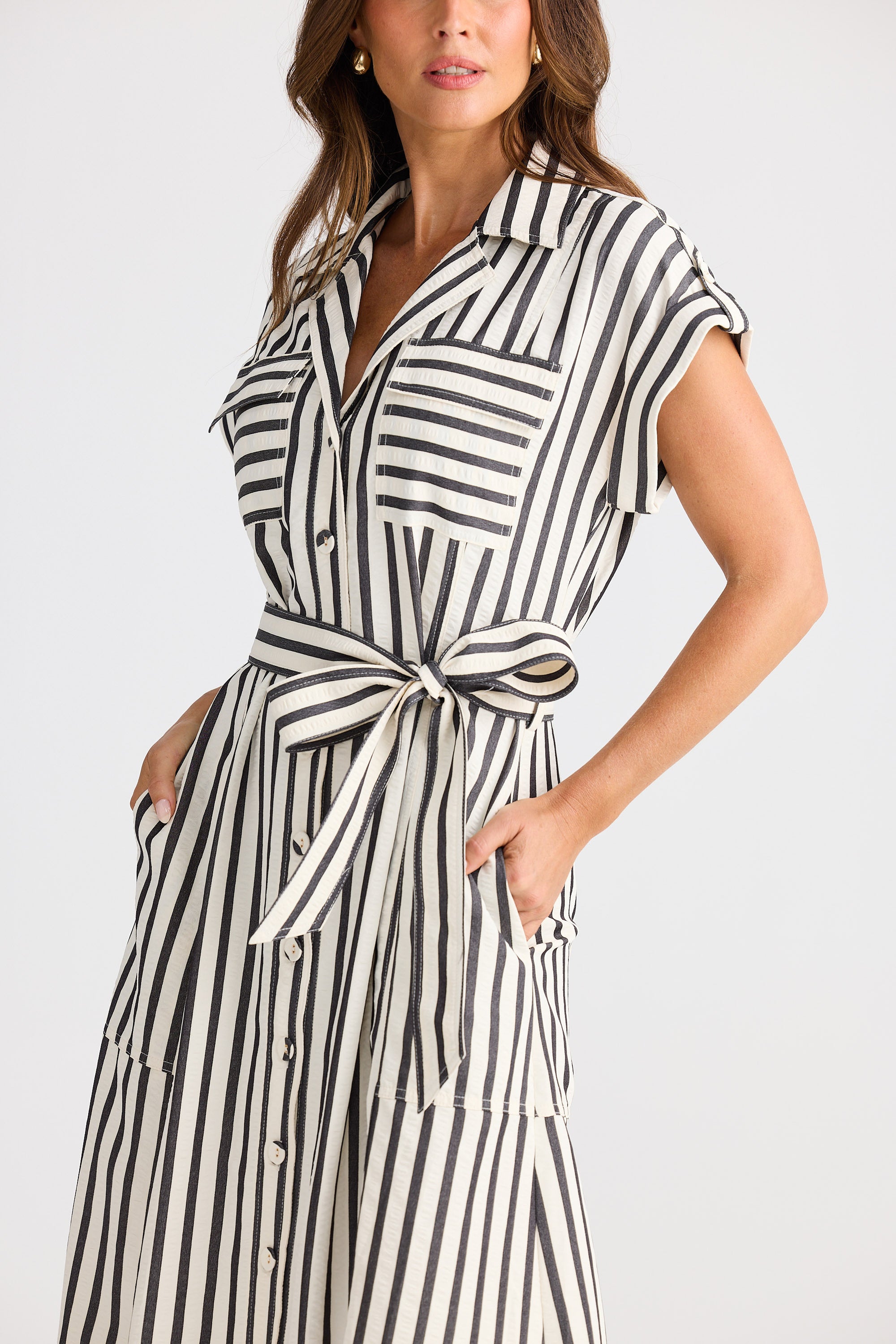 Woman wearing a black and white striped dress with a belt on a plain background